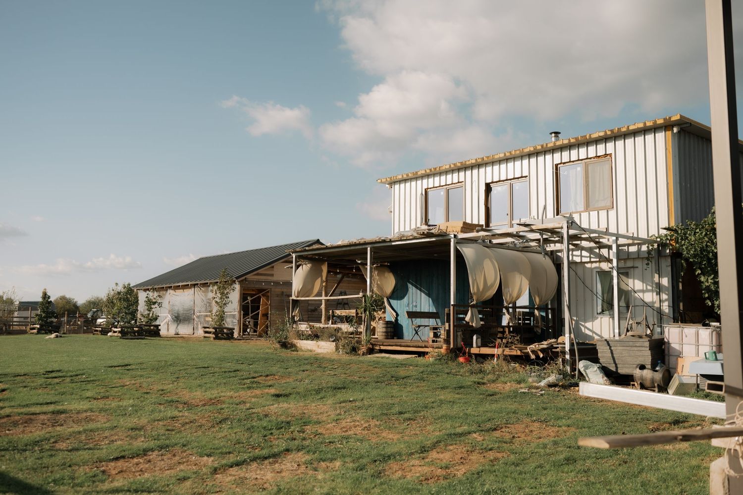 Panoramic view of metal storage buildings and barns on a rural property with green pastures under blue skies.