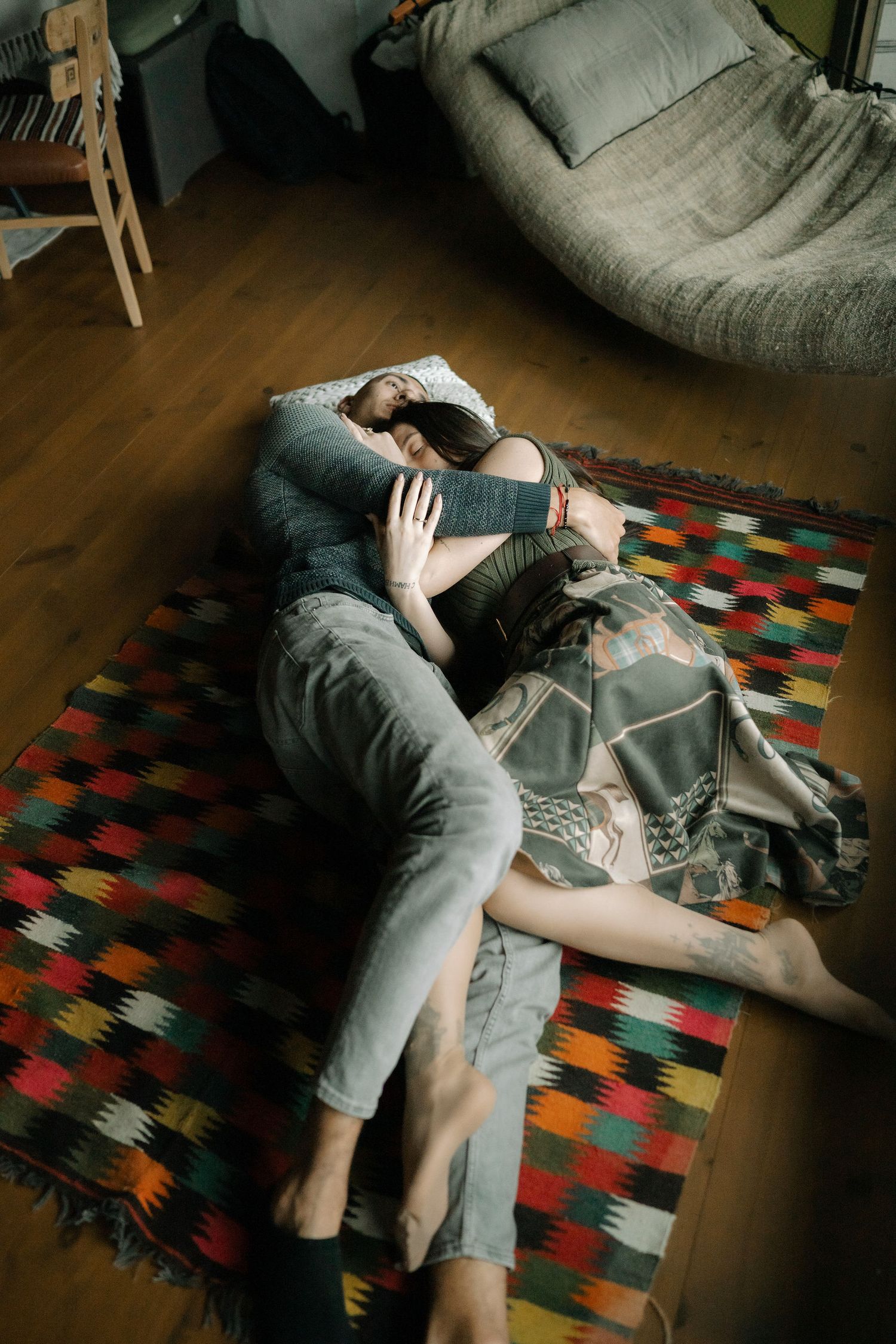 Person lying on a colorful geometric patterned rug while reading a book in dim lighting.