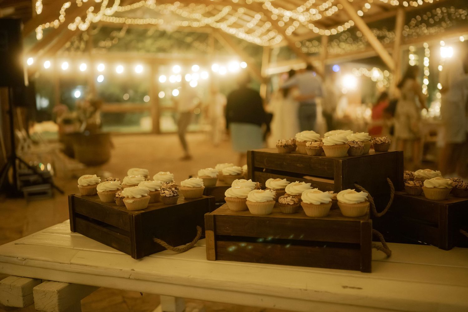 String lights illuminate a rustic wooden table setting with glowing candles and decorative elements at an evening event.