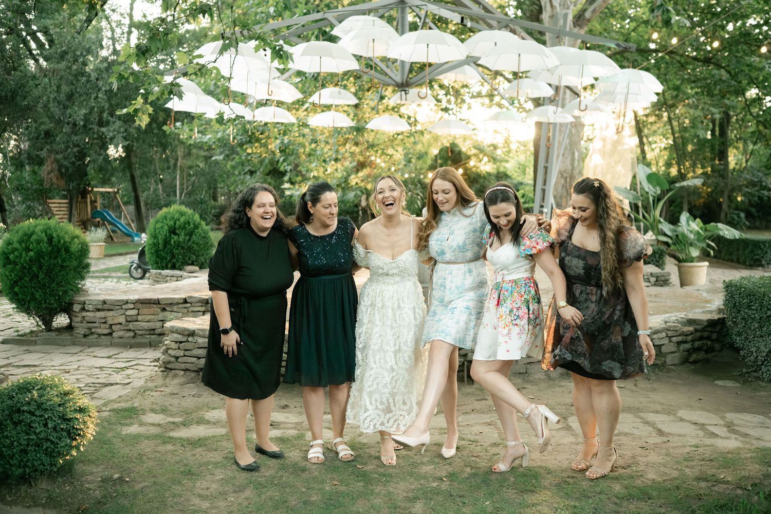 A group of people in formal attire gather outdoors for a wedding celebration in a garden setting.