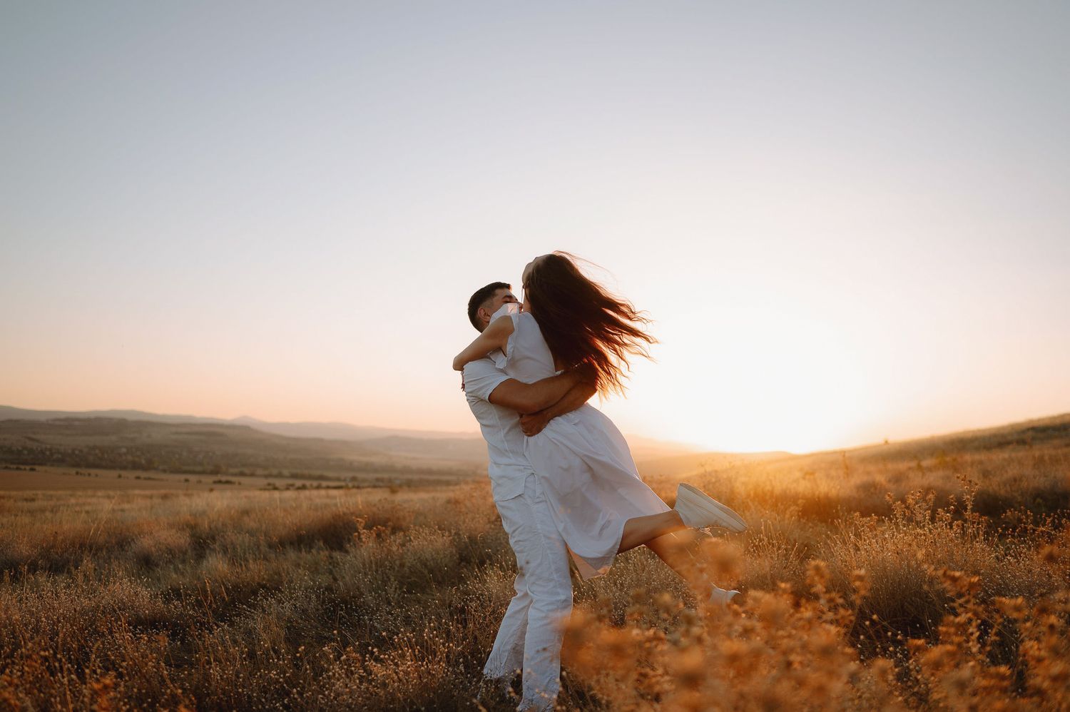 A romantic couple embraces in a golden wheat field during sunset creating a dreamy silhouette against the warm sky.