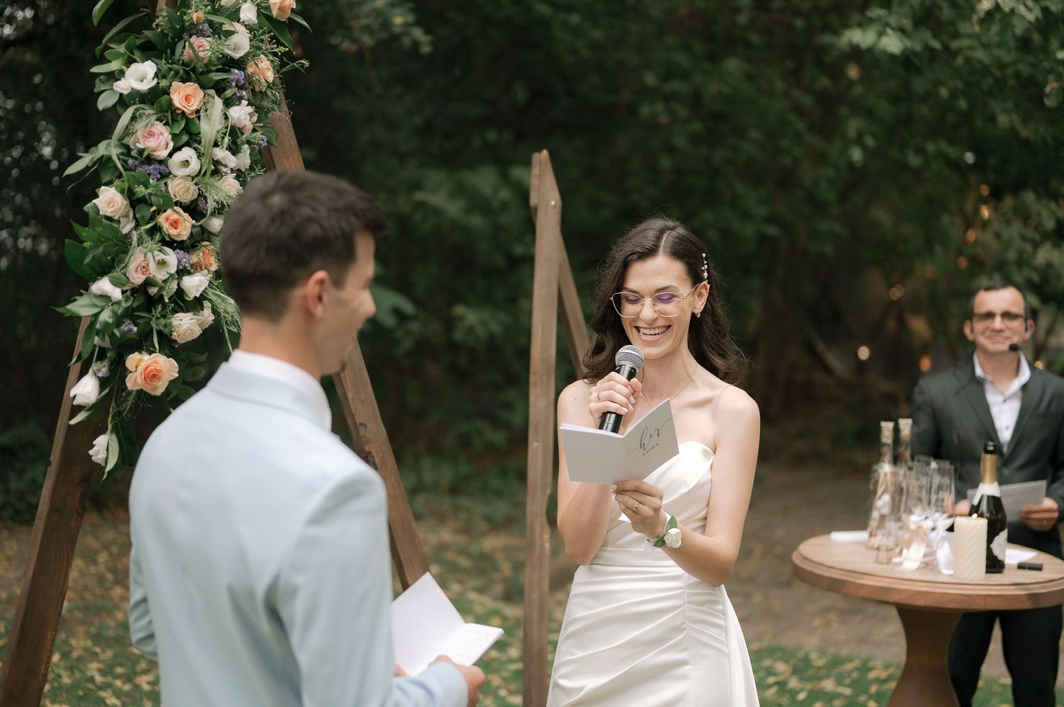A couple exchanges vows during an outdoor garden wedding ceremony beneath a floral arch with peach roses.