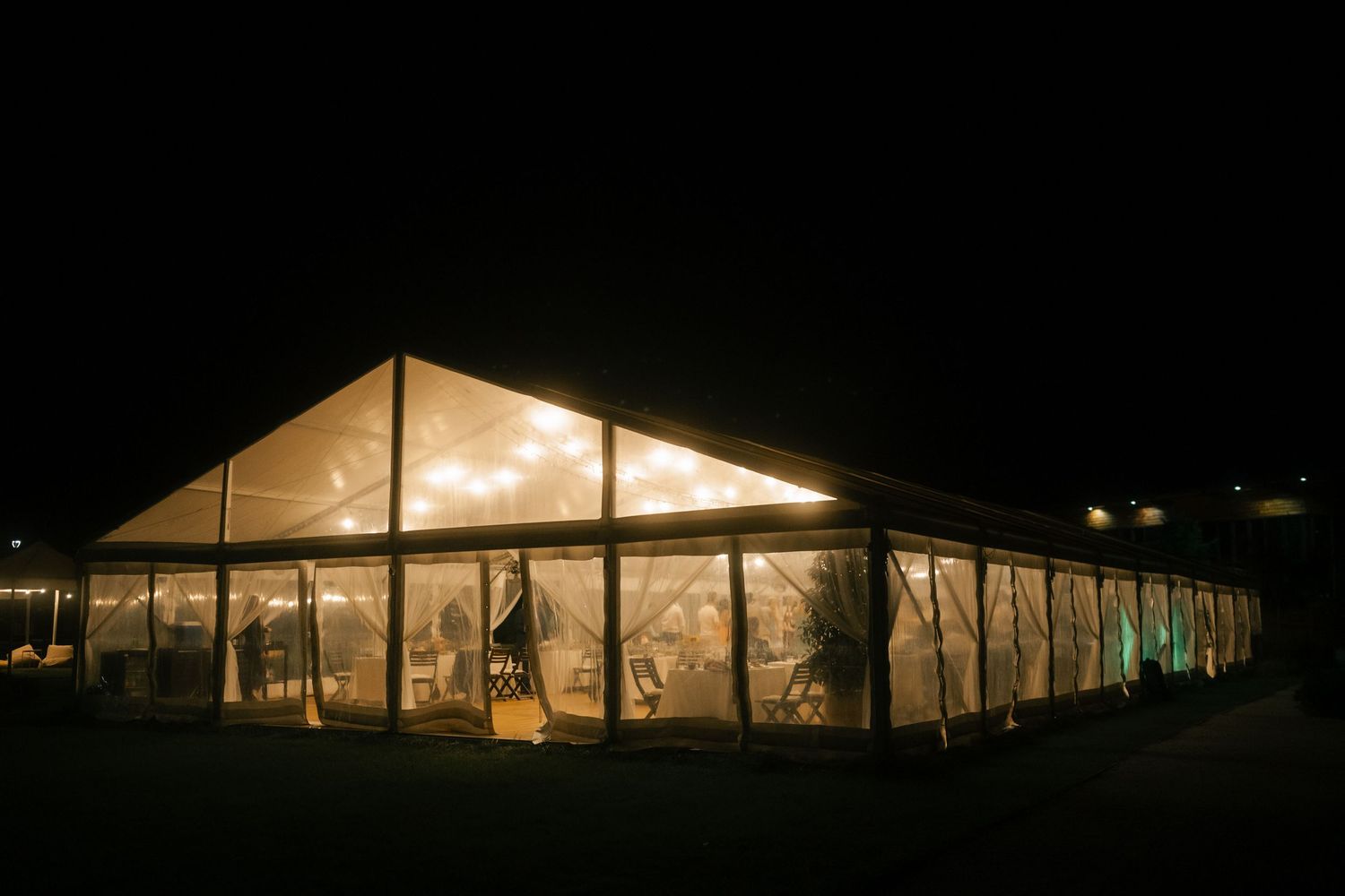Large white reception tent glowing from within against dark night sky with panoramic view.