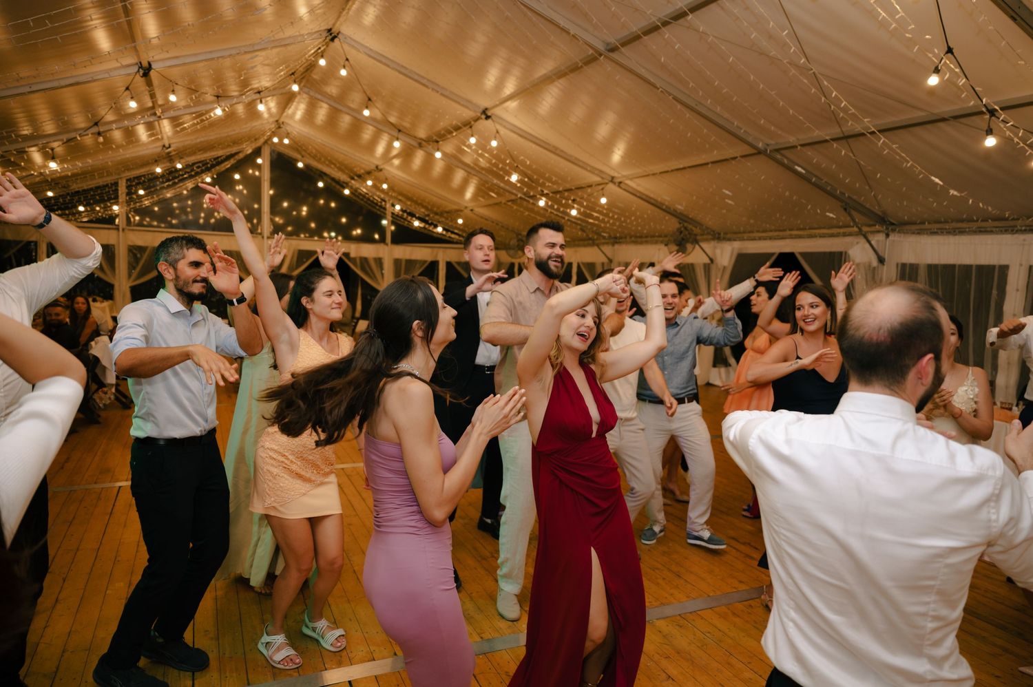 Wedding guests dancing and celebrating under a tent decorated with string lights at an evening reception.