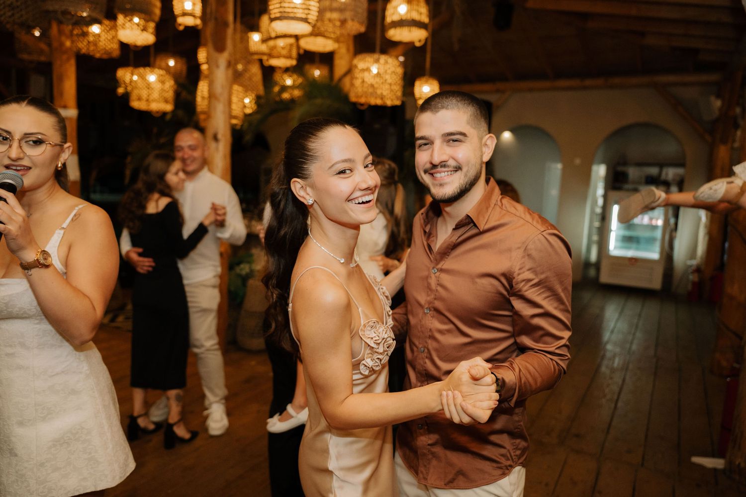 Couples dancing together at a rustic wedding reception venue with warm lighting and wooden floors.