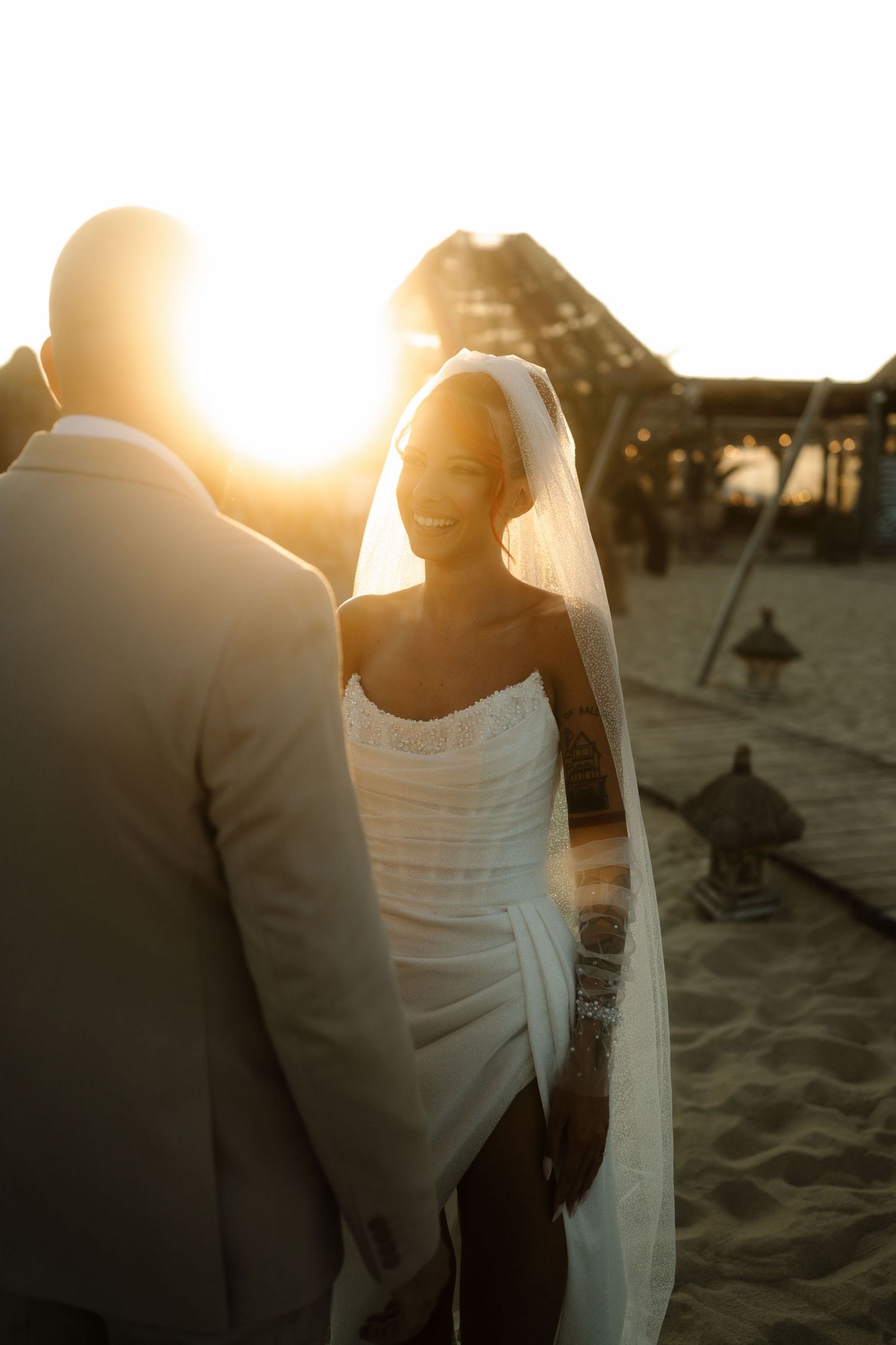 A couple on the beach at sunset with the bride wearing a white dress and flowing veil.
