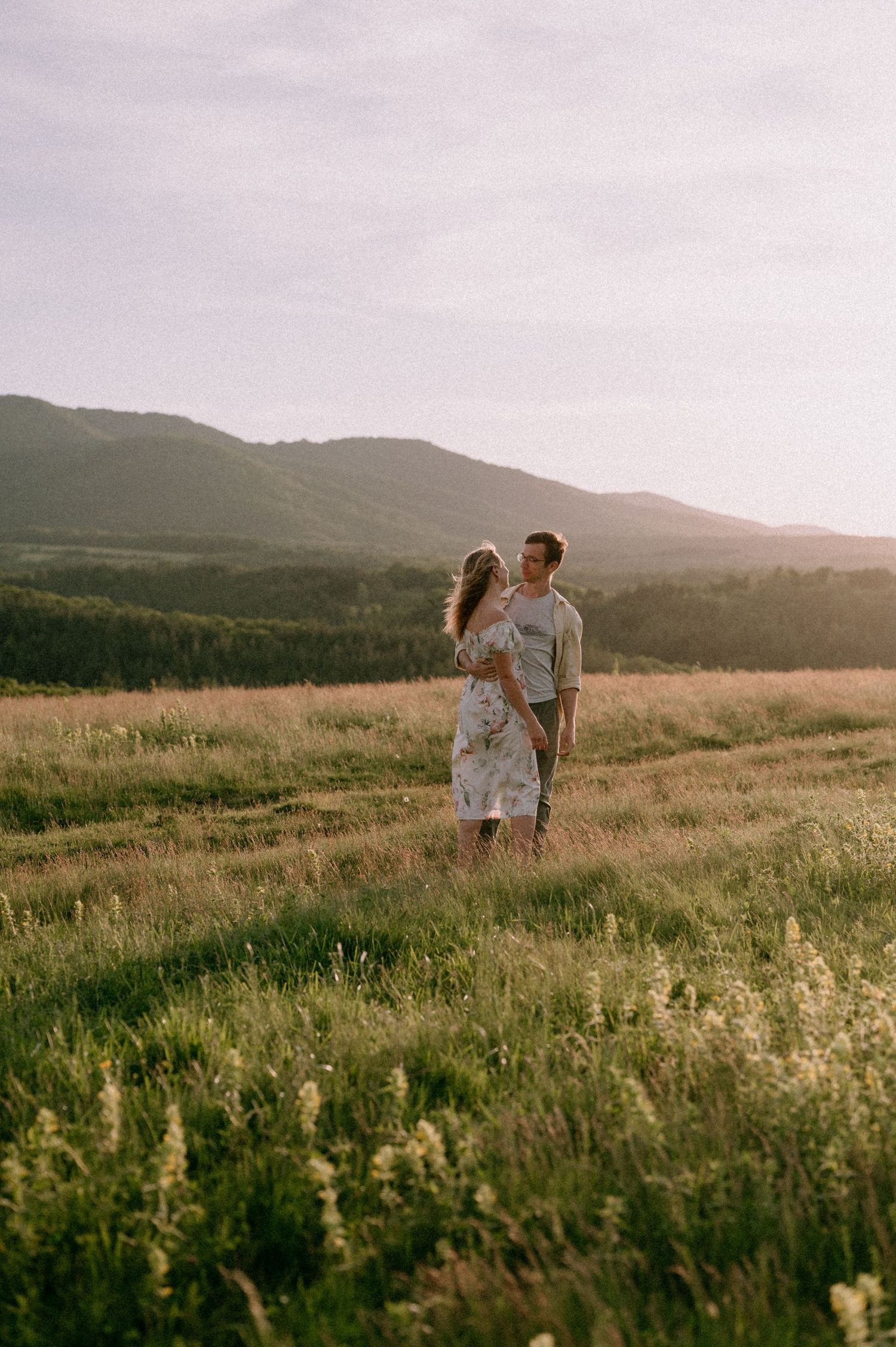 Loving pair share intimate moments while standing in a wildflower meadow with mountains in background.