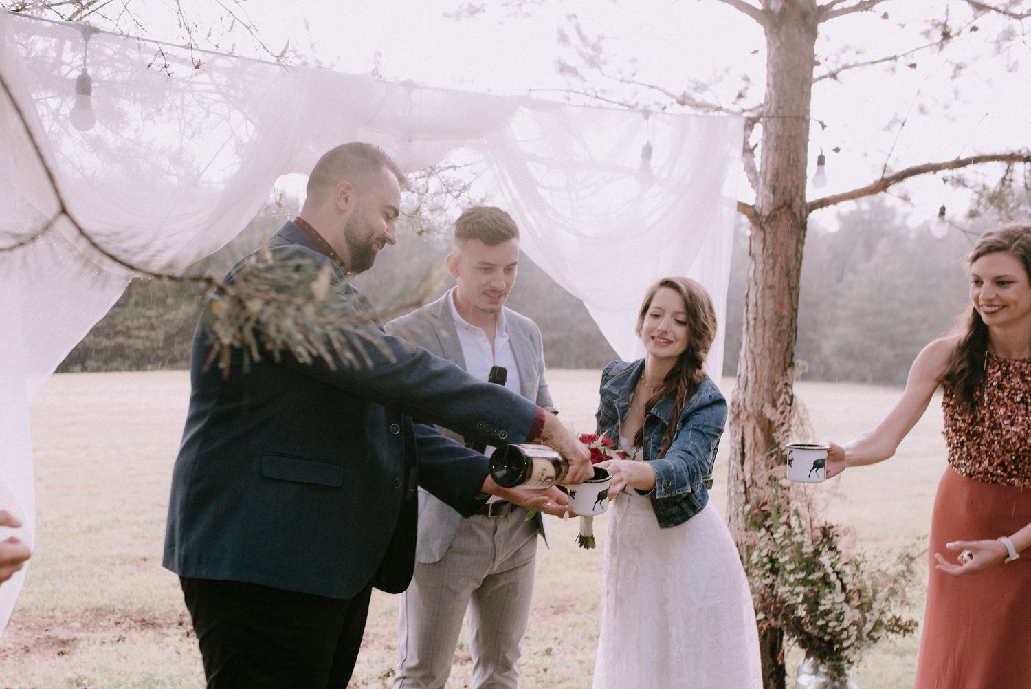 Outdoor wedding ceremony with white fabric backdrop and natural pine tree setting.
