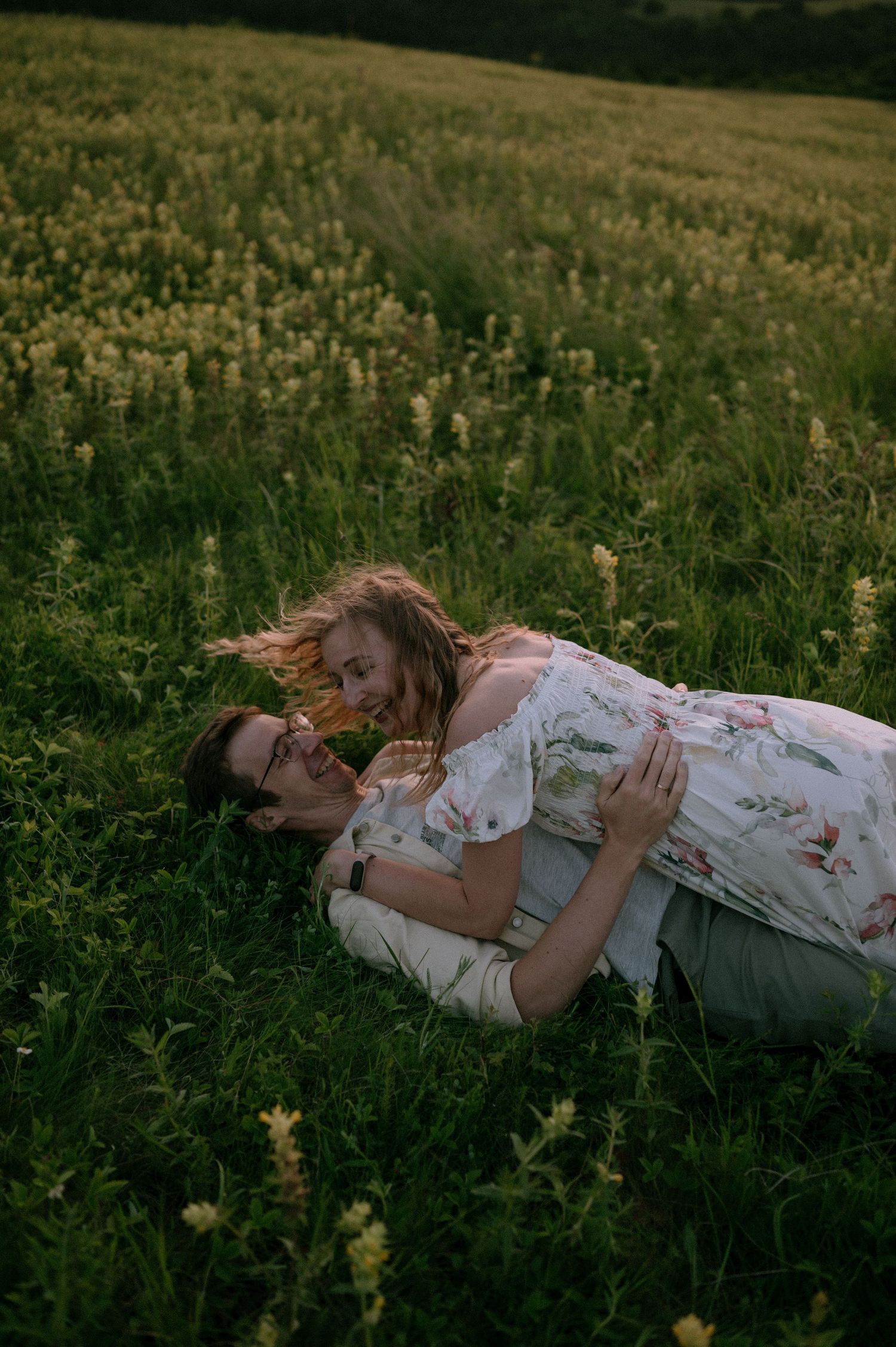 Two people share an intimate moment while lying in a field of tall grass and flowers.