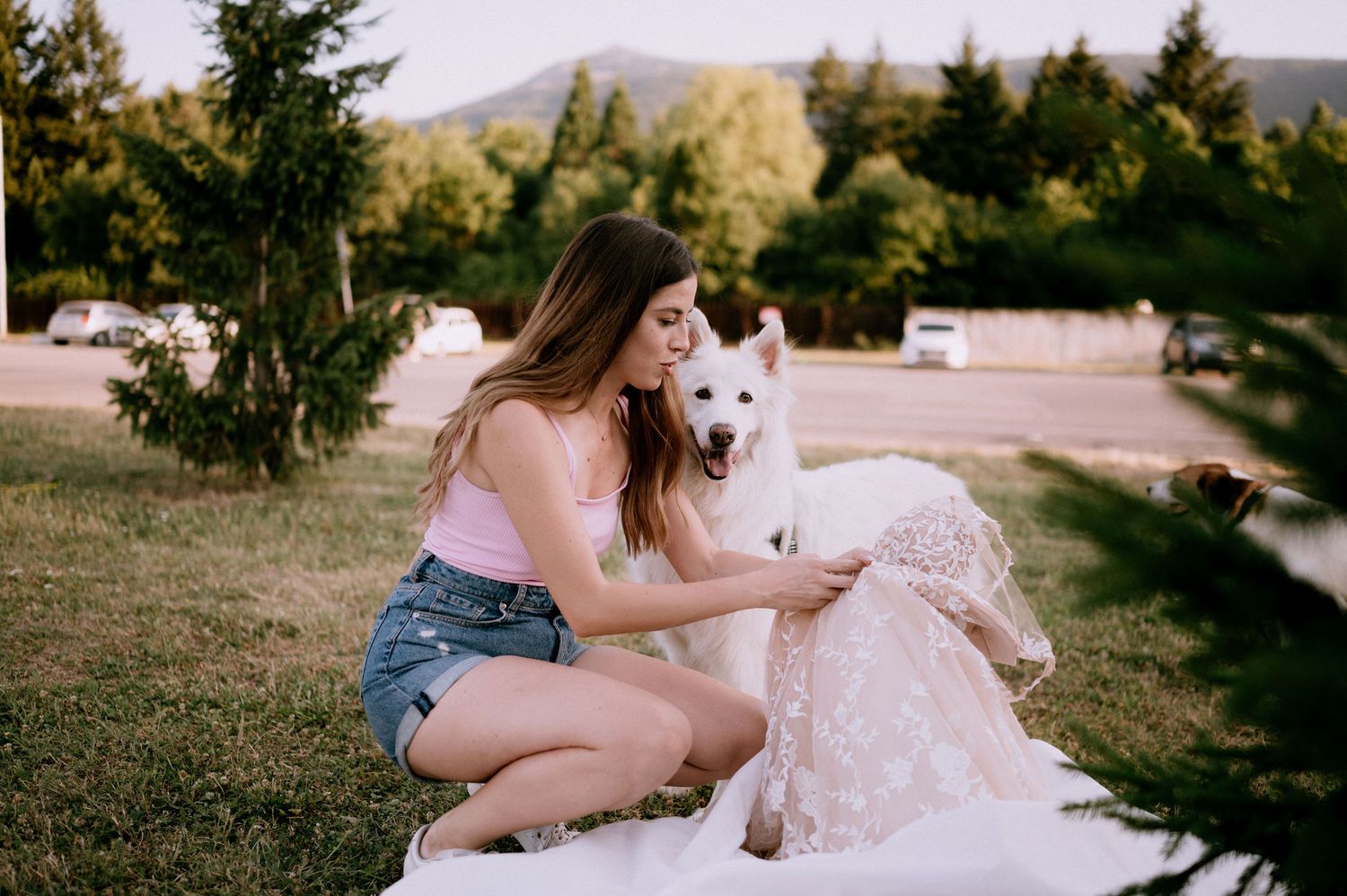 A person in a white dress relaxes on grass with a fluffy white dog in a natural setting.