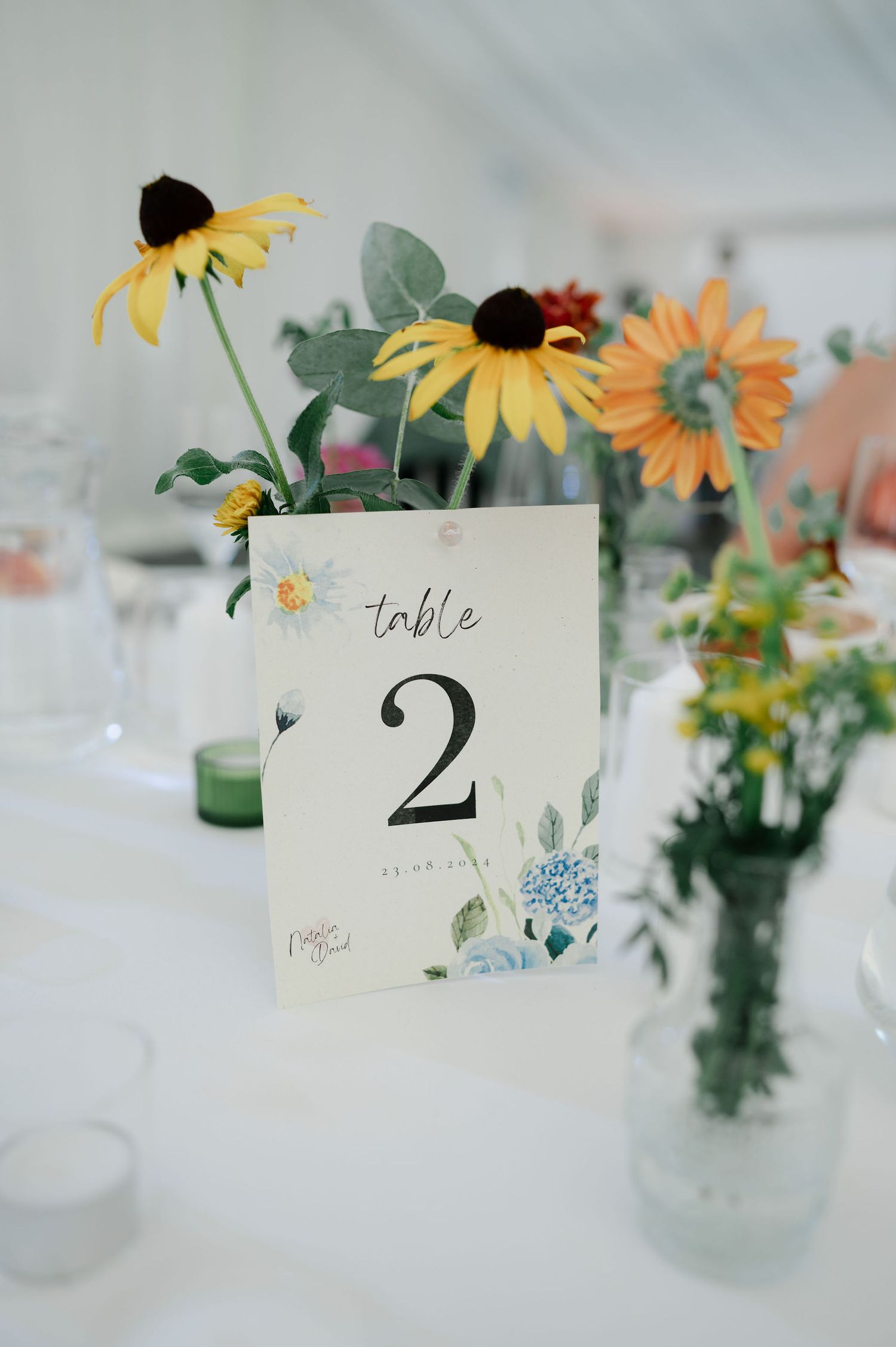 Table number two card displayed with yellow sunflowers and wildflowers in glass vases.