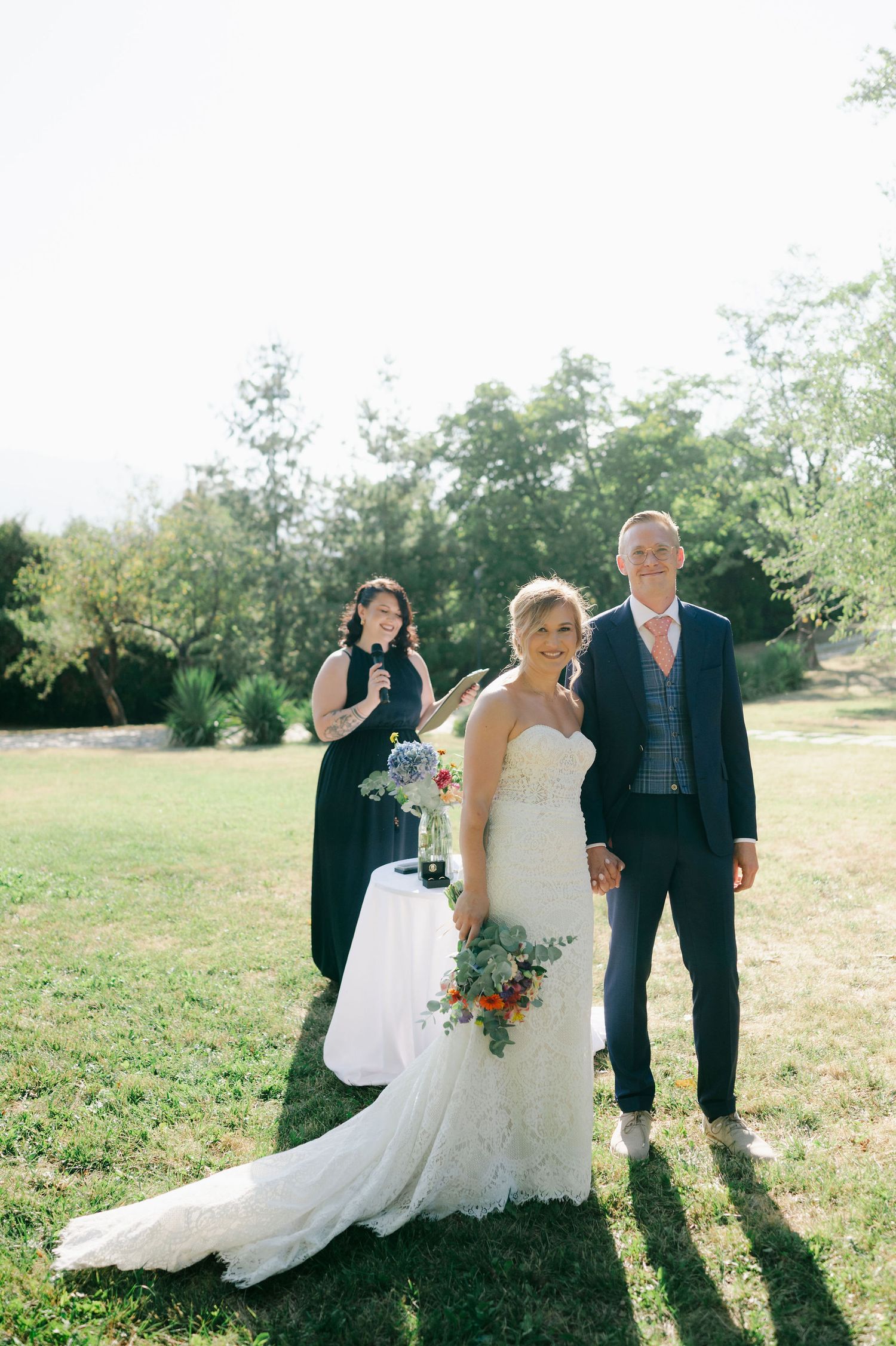 Wedding party poses together casting long shadows on grassy field.