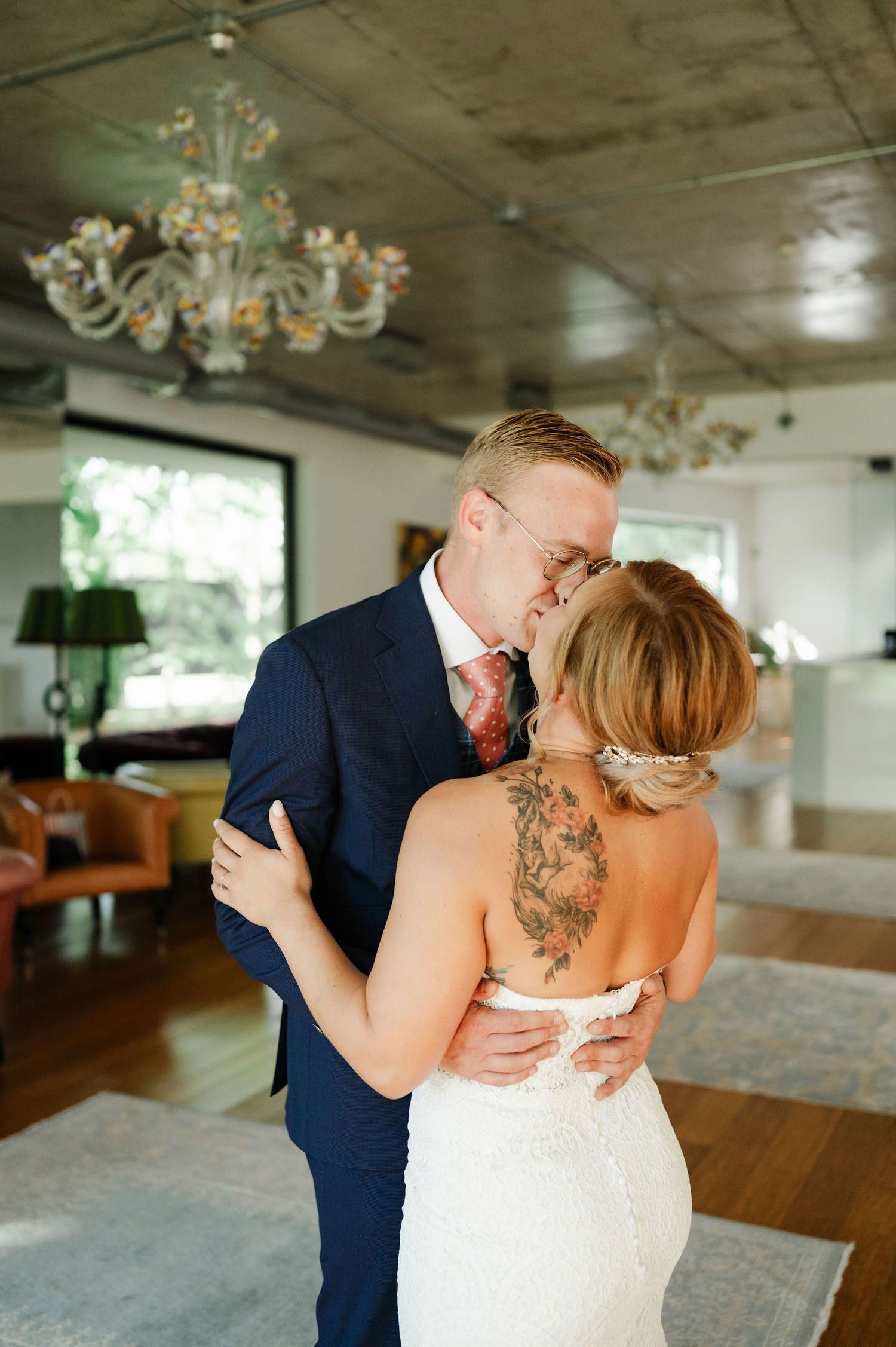 A romantic wedding moment unfolds in an elegant venue with hardwood floors and chandeliers.