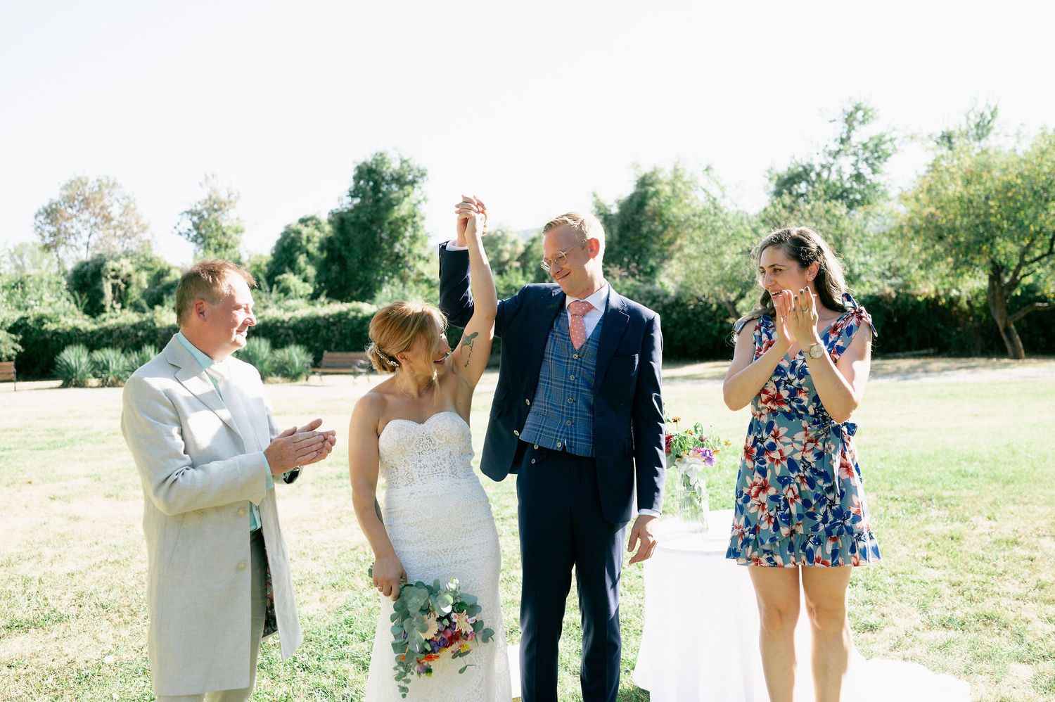 Wedding guests interact playfully on a grassy lawn during an outdoor celebration.