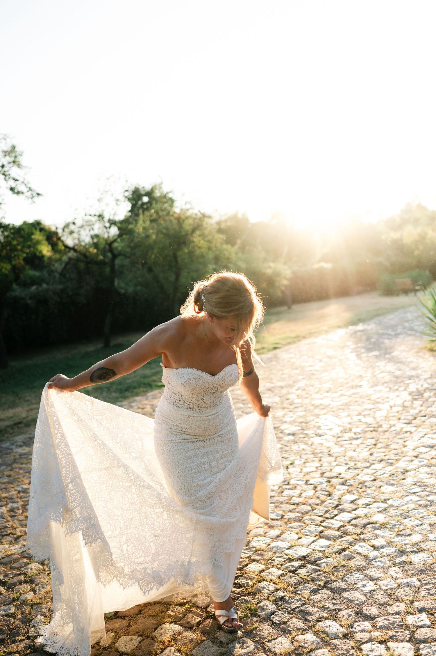 Romantic bridal moment captured with dress movement on cobblestone path at golden hour.