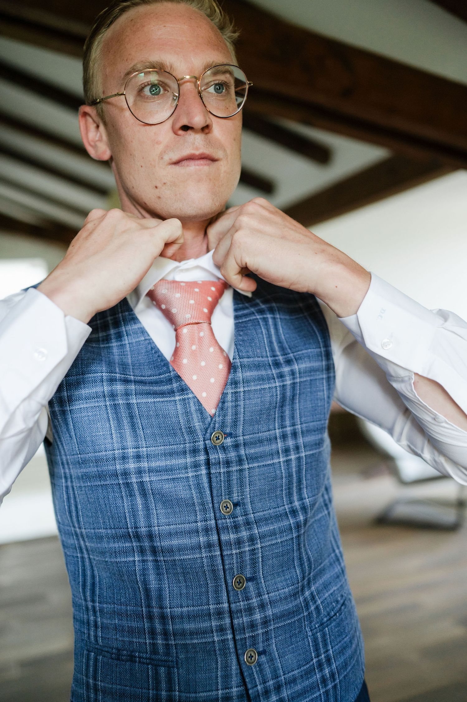 Close-up shot of someone adjusting their collar while wearing a blue plaid vest.