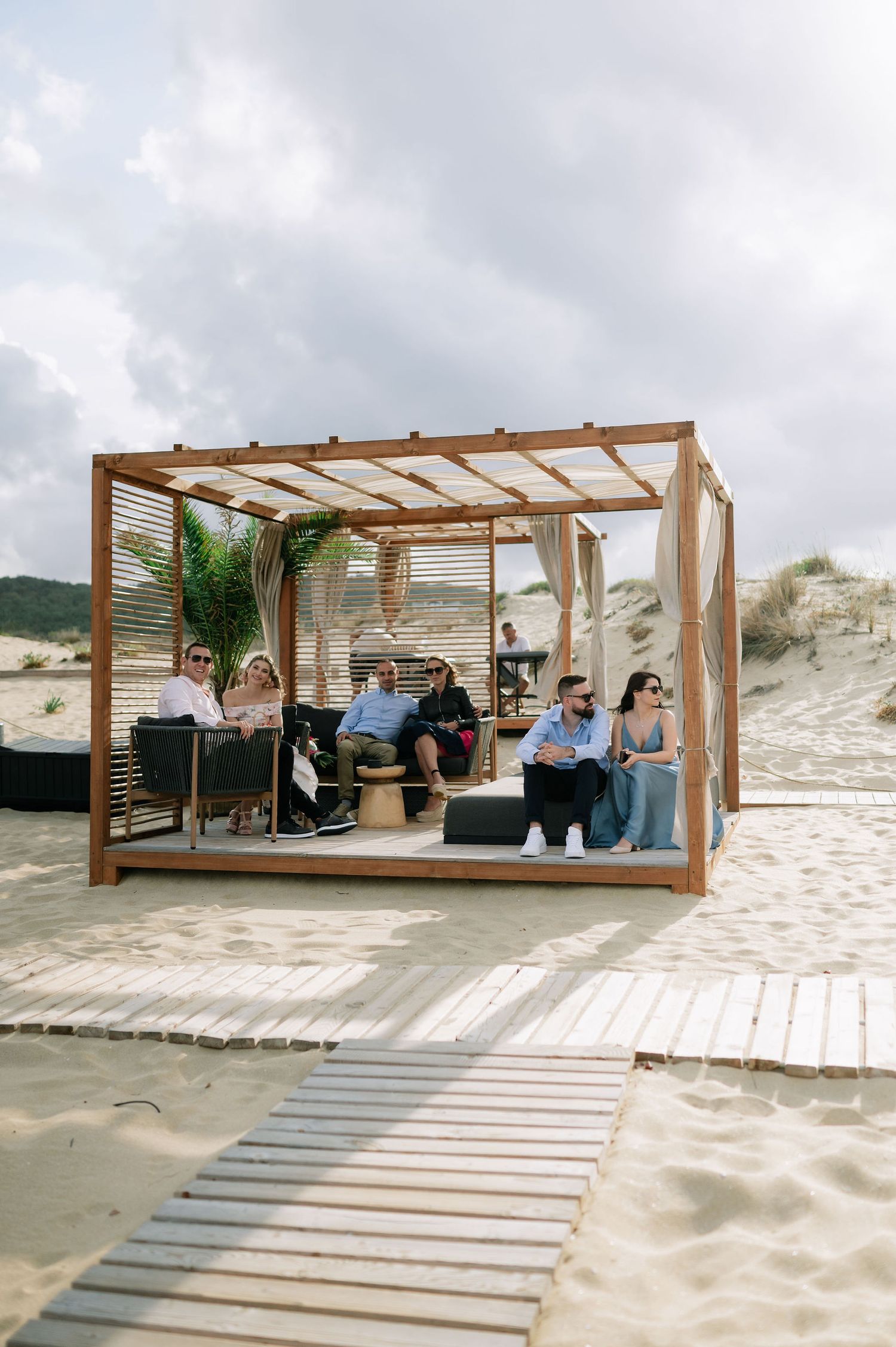 Beach lounge area with wooden pergolas and boardwalk stretching across the sand.