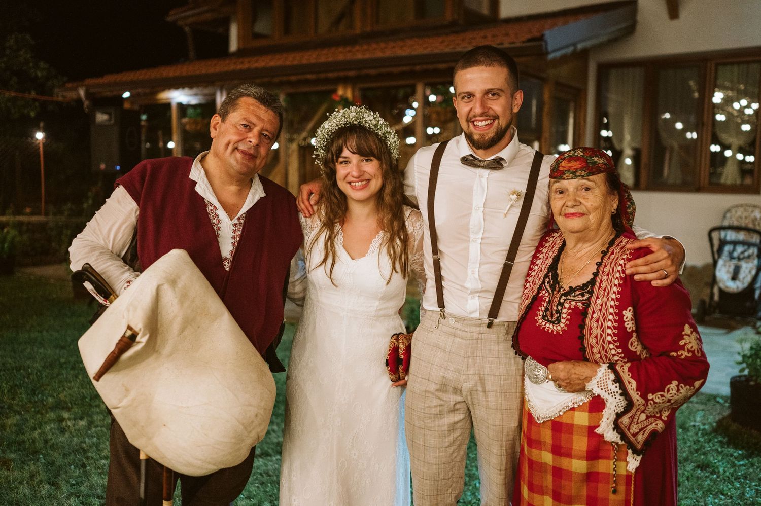 Wedding guests in vintage-inspired attire celebrate at an outdoor reception with string lights and rustic decor.