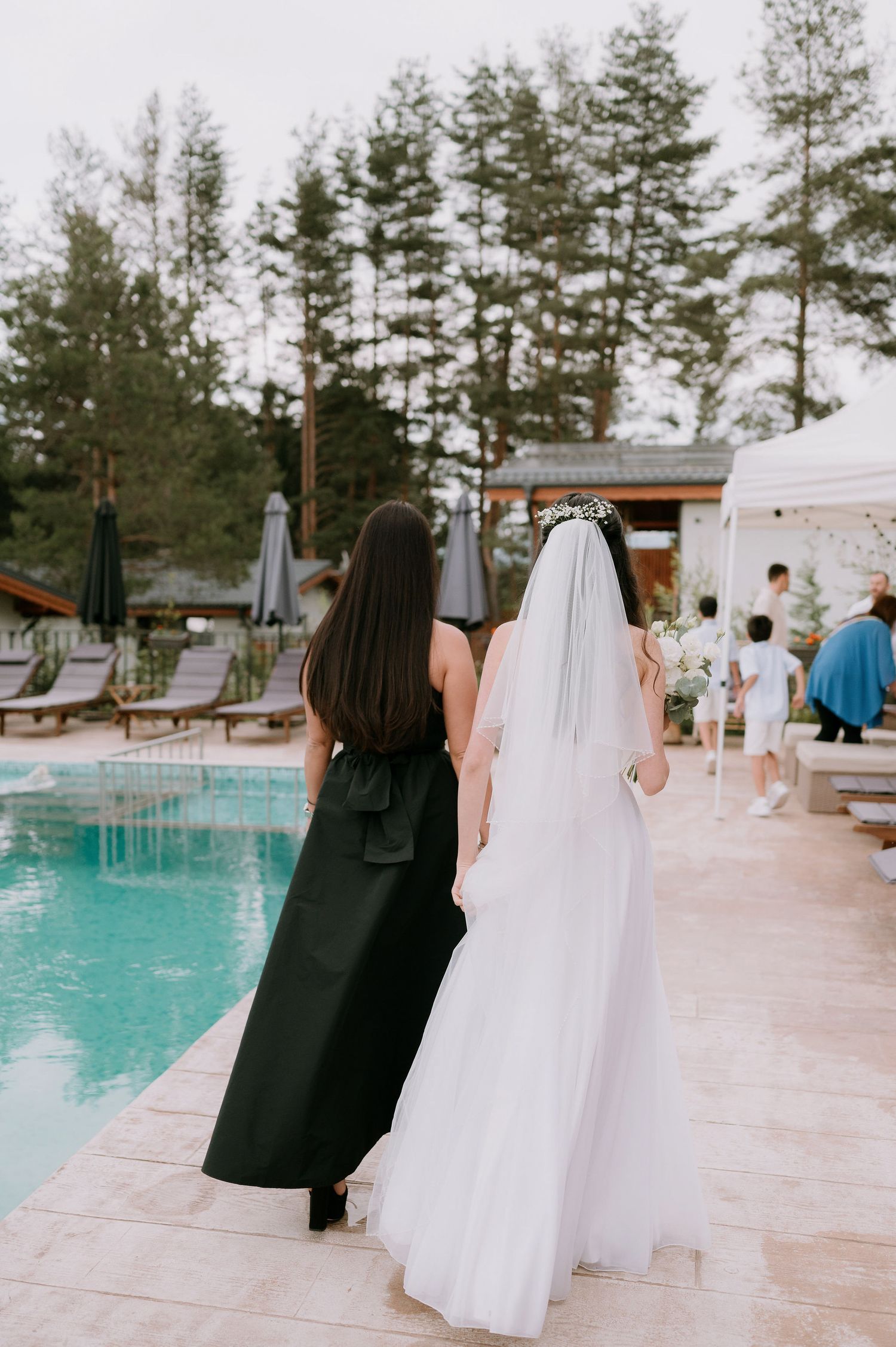 Two people in black and white outfits walking beside a turquoise pool at an outdoor venue.