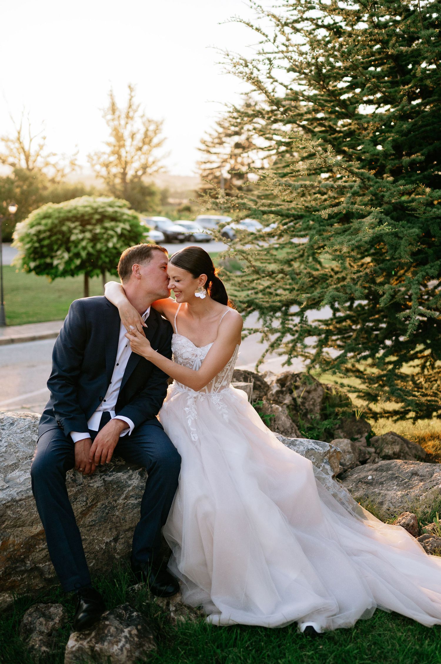 Romantic sunset portrait of wedding couple embracing on decorative garden rocks.