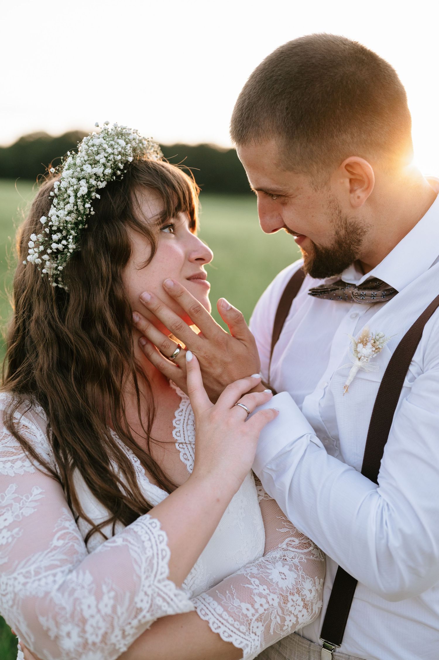 Tender moment between newlyweds at sunset with bride wearing lace dress and floral crown.