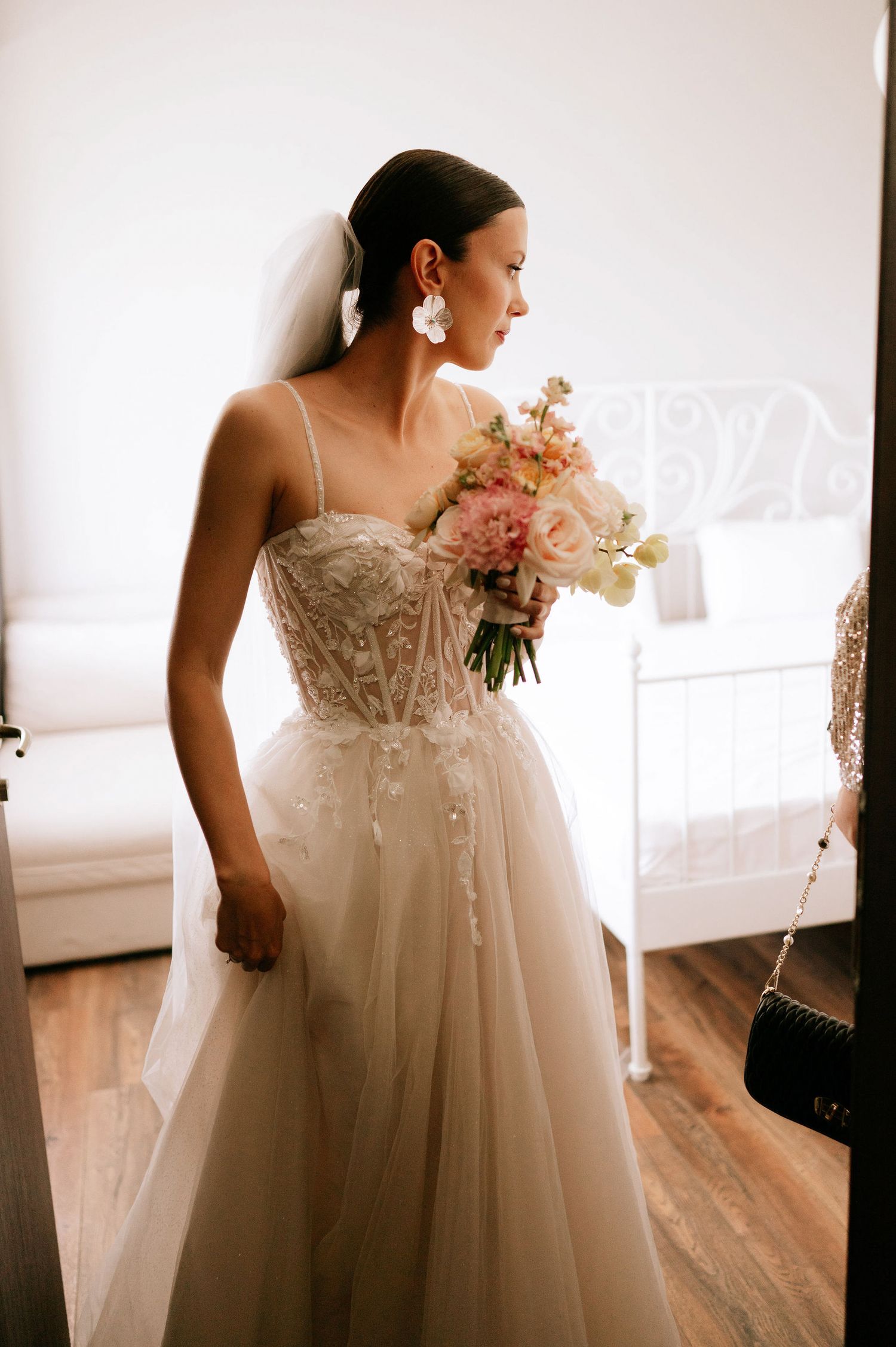 Elegant bride in a flowing white lace gown with intricate bodice details indoors.