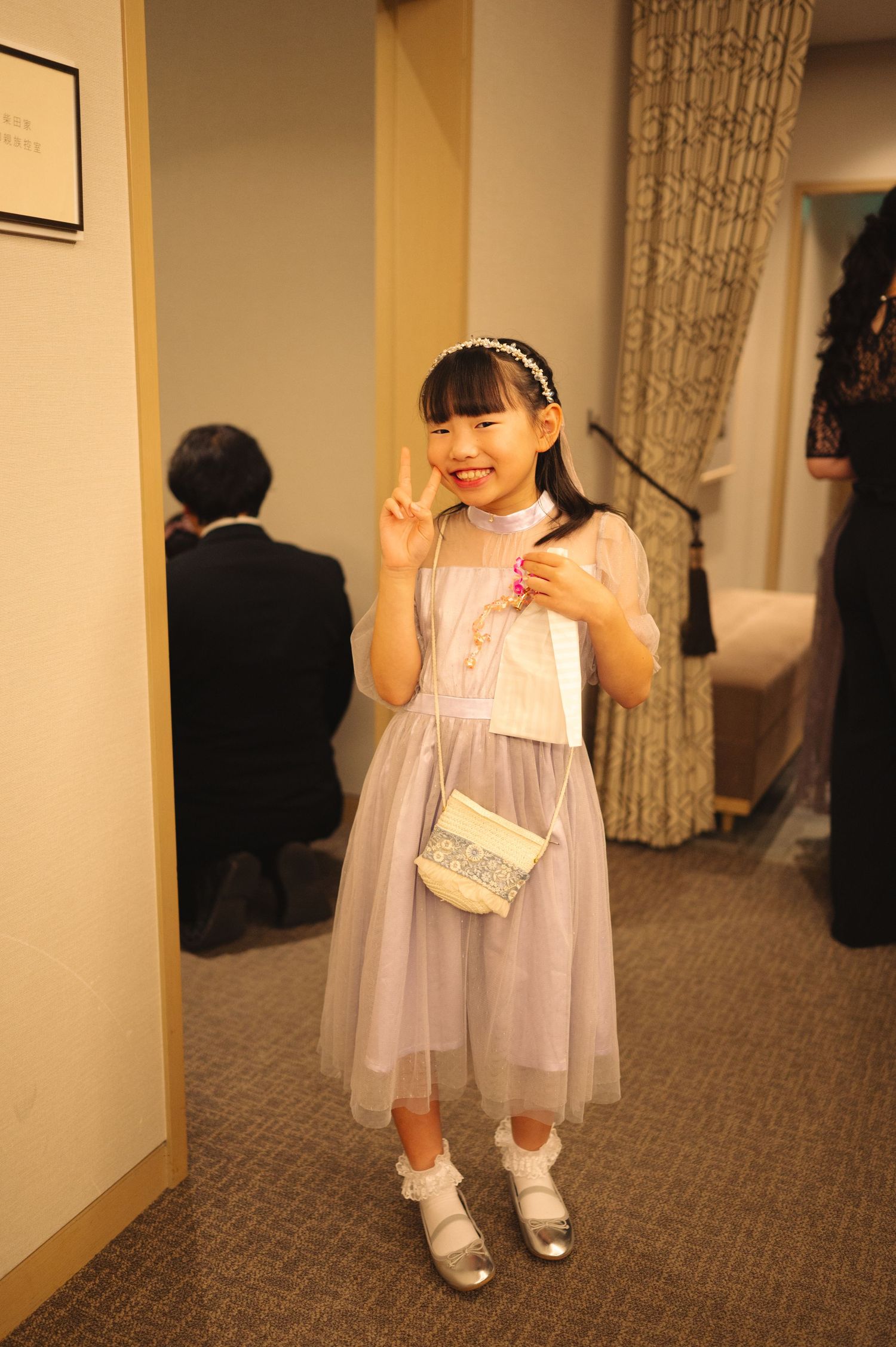 A young flower girl in a white dress and matching accessories at a formal event.
