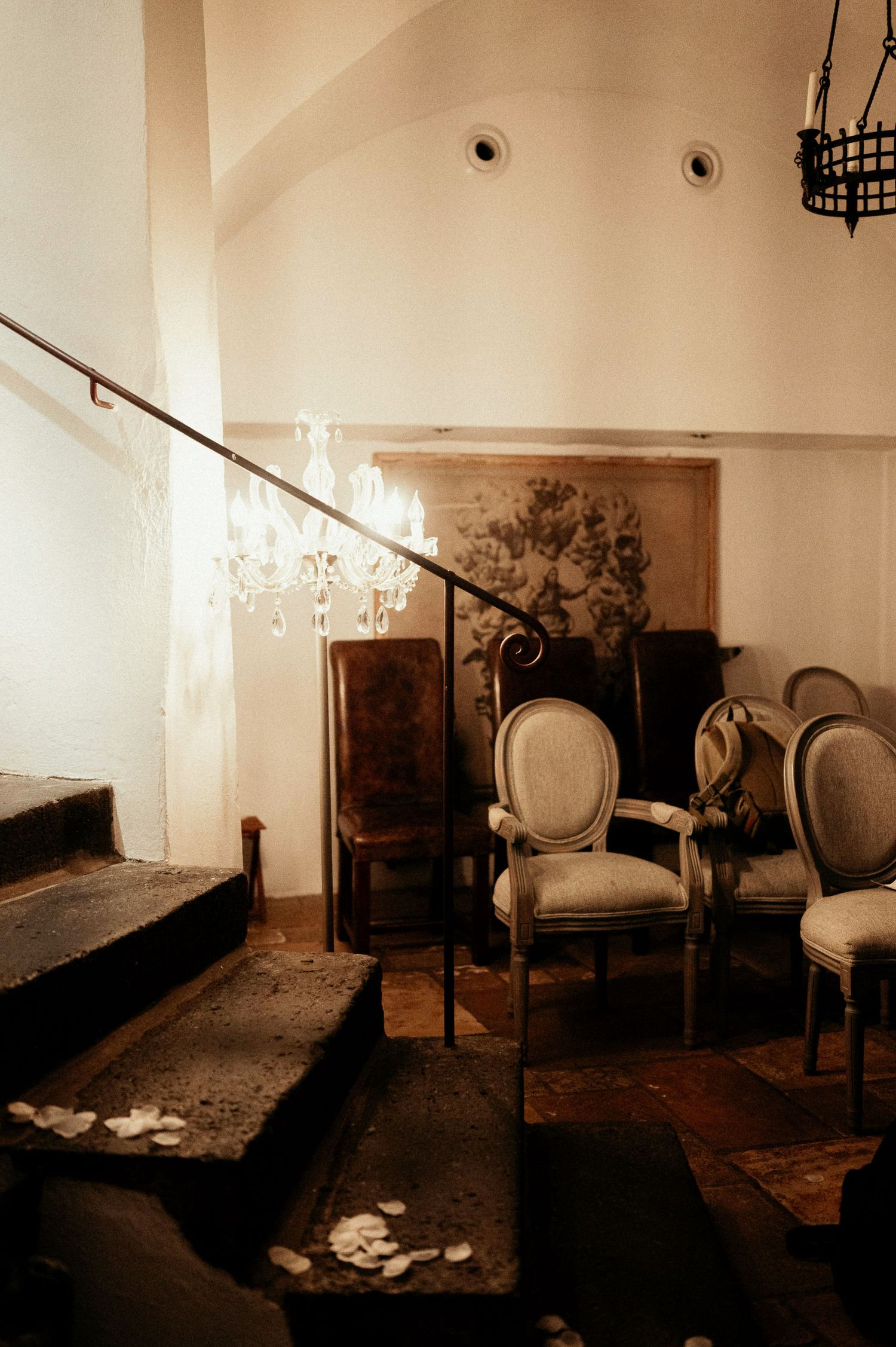 Antique furnished room with classic chairs and scattered rose petals on hardwood floor.
