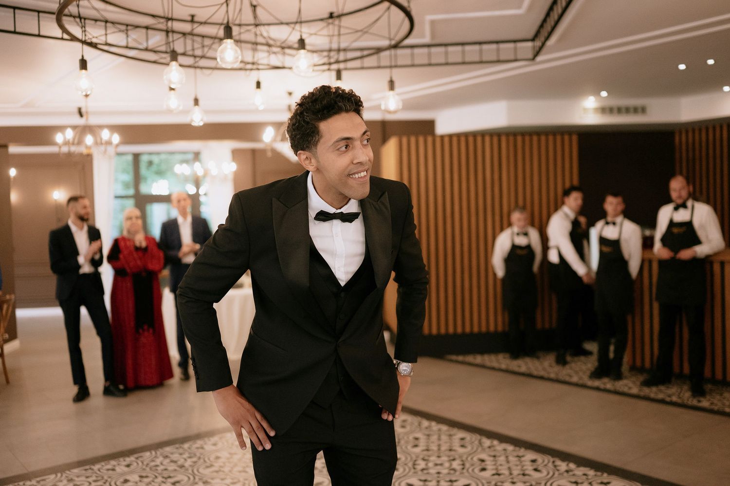 Wedding guests mingling in an elegant reception hall with modern lighting and wood accents.