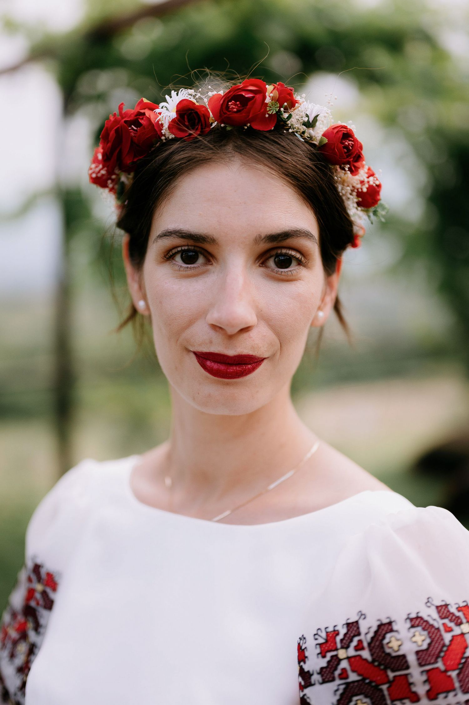Side profile portrait wearing red floral crown and white dress with traditional embroidery.