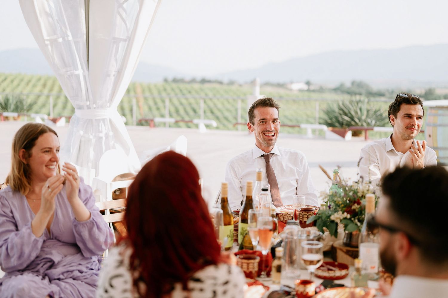Panoramic view of wedding guests dining in a tent with vineyard backdrop.