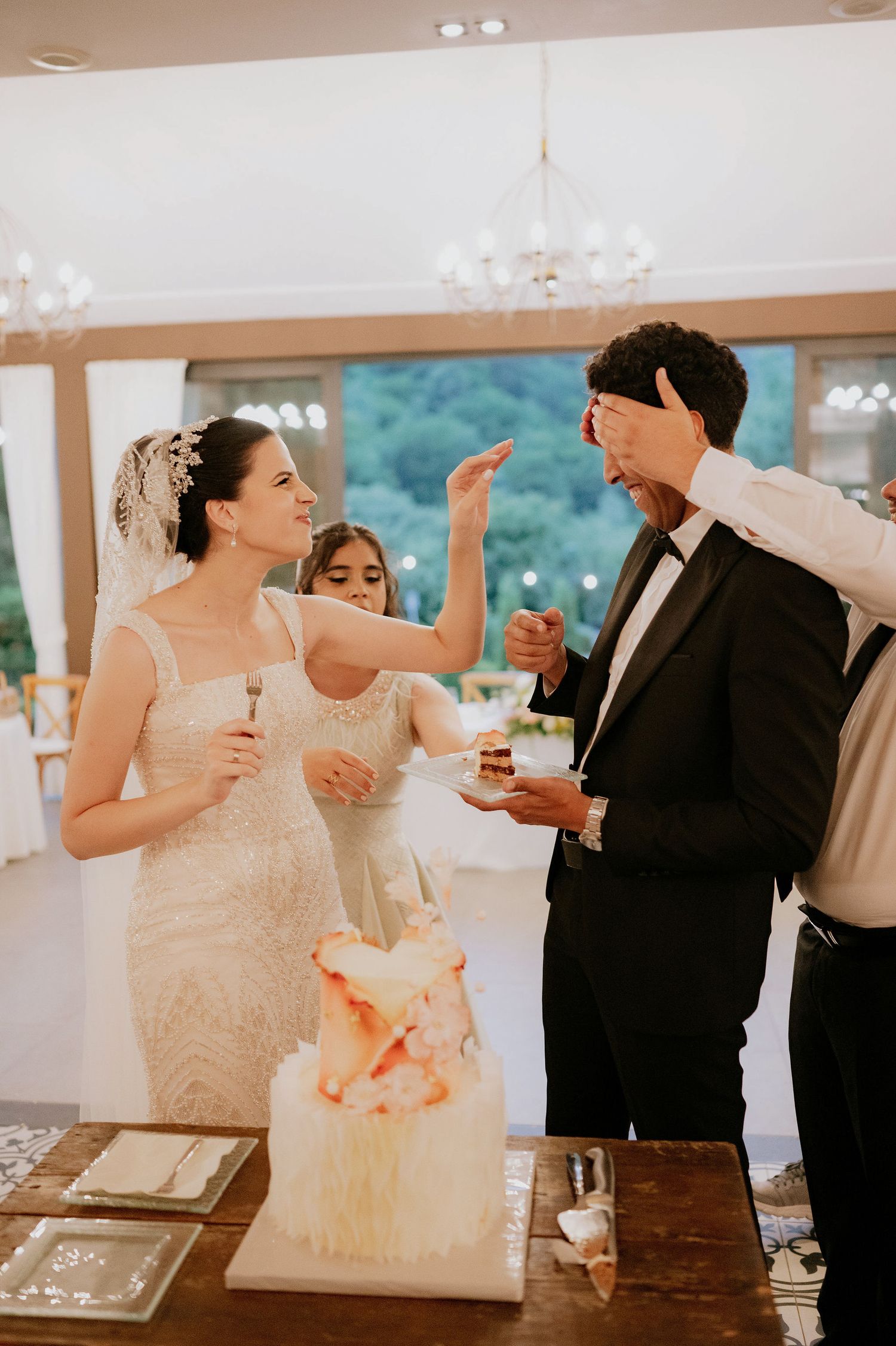 Wedding cake cutting ceremony in an elegant indoor venue with chandeliers.