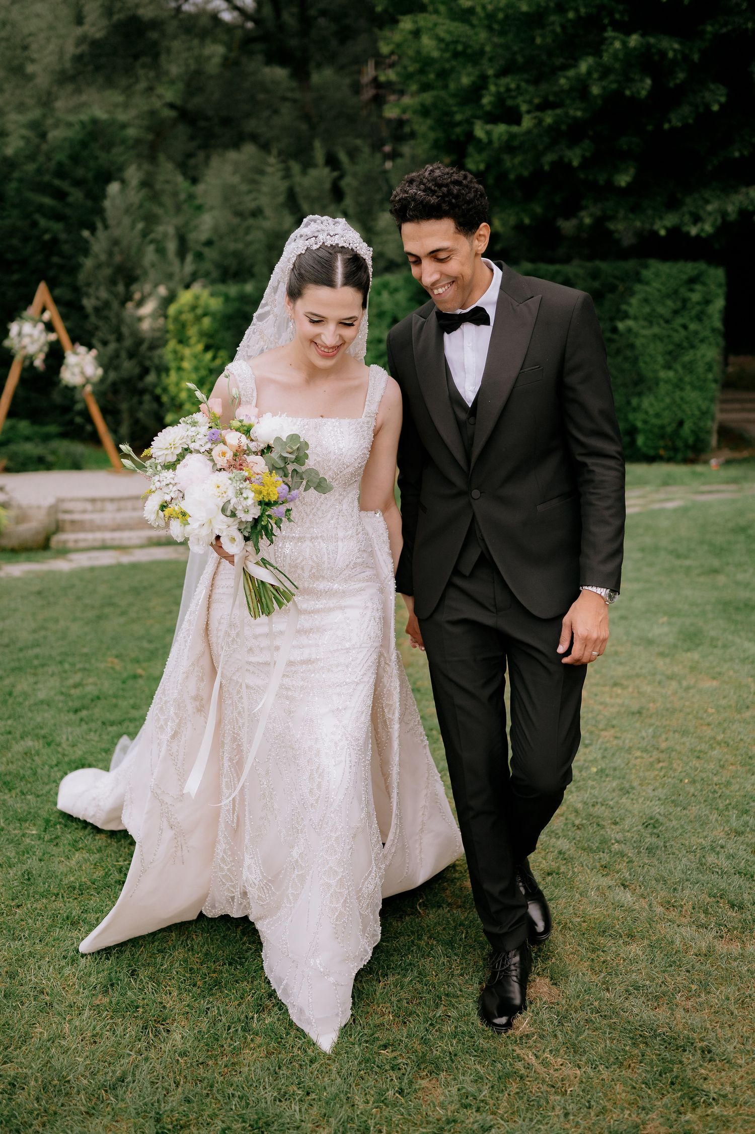 Wedding couple strolling on a lawn with the bride's dress and veil flowing elegantly.