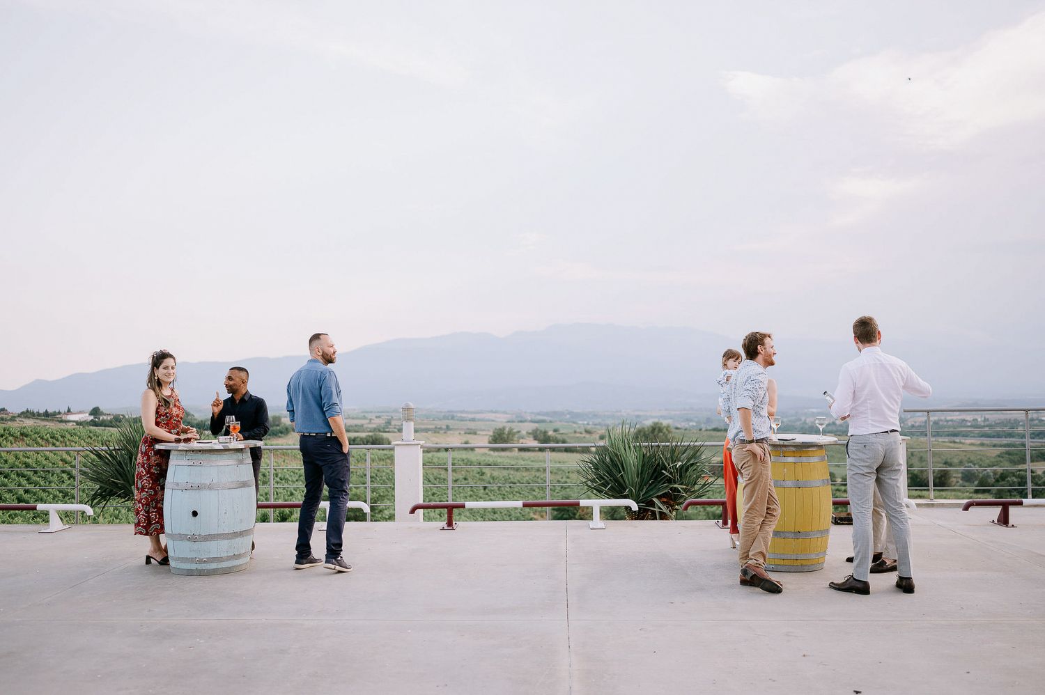 People enjoying a gathering on an outdoor terrace overlooking a scenic valley.