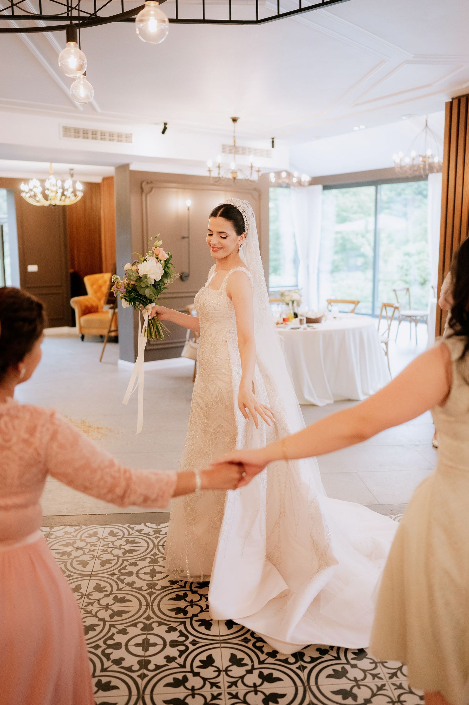 Bridesmaids in blush pink dresses admire a wedding gown in an elegant reception venue with patterned floors.