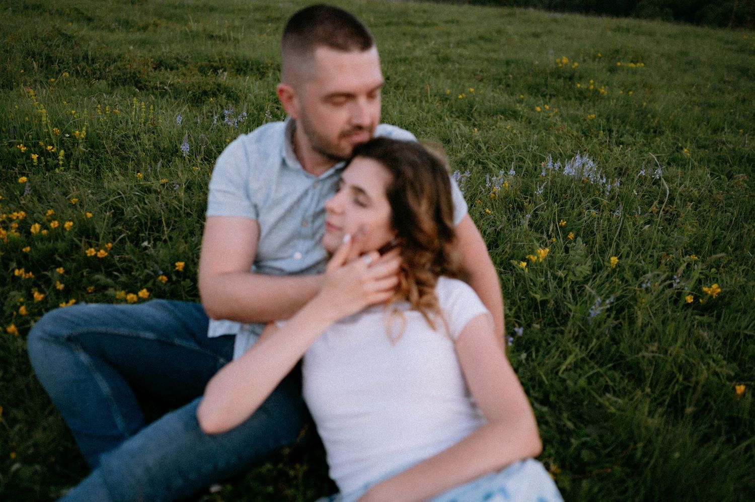 Romantic couple sharing an intimate moment while sitting in a wildflower meadow at sunset.