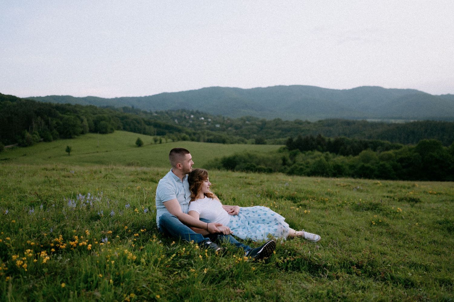 Two people share an intimate moment while lying in a mountain meadow.