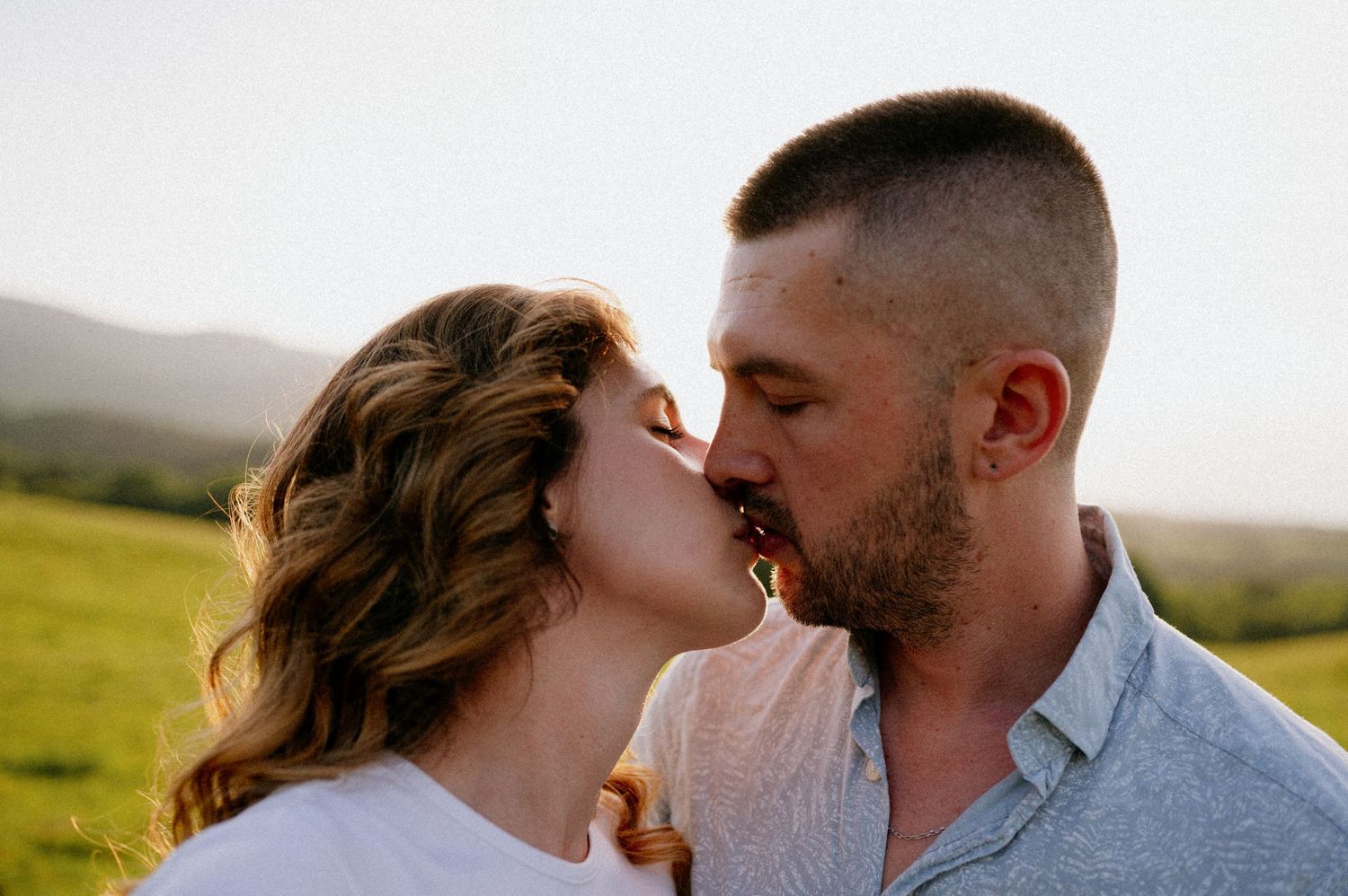 Close-up of a tender kiss between couple in a grassy field at sunset.