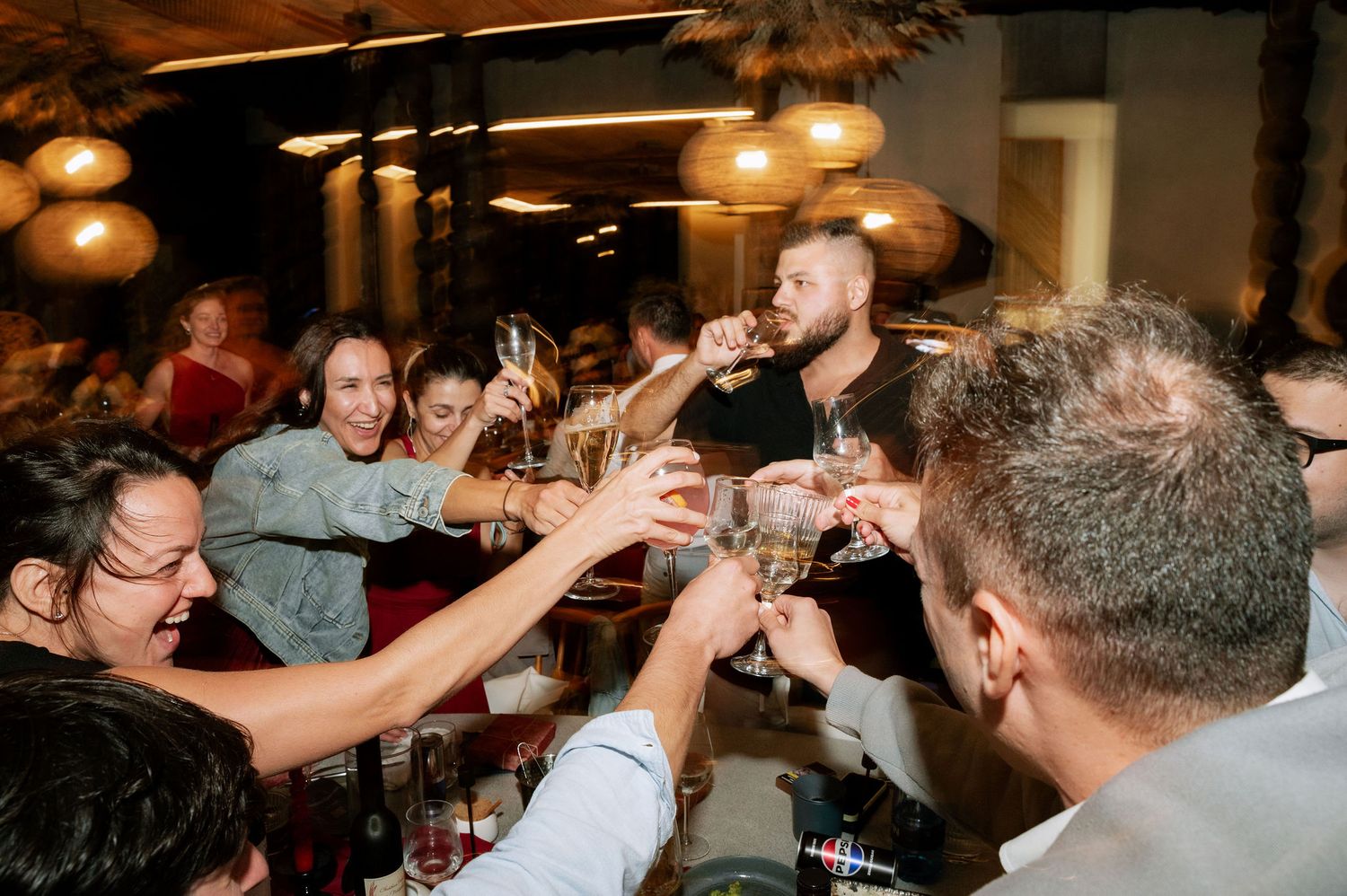 Friends raising glasses in a celebratory toast at a lively restaurant gathering.