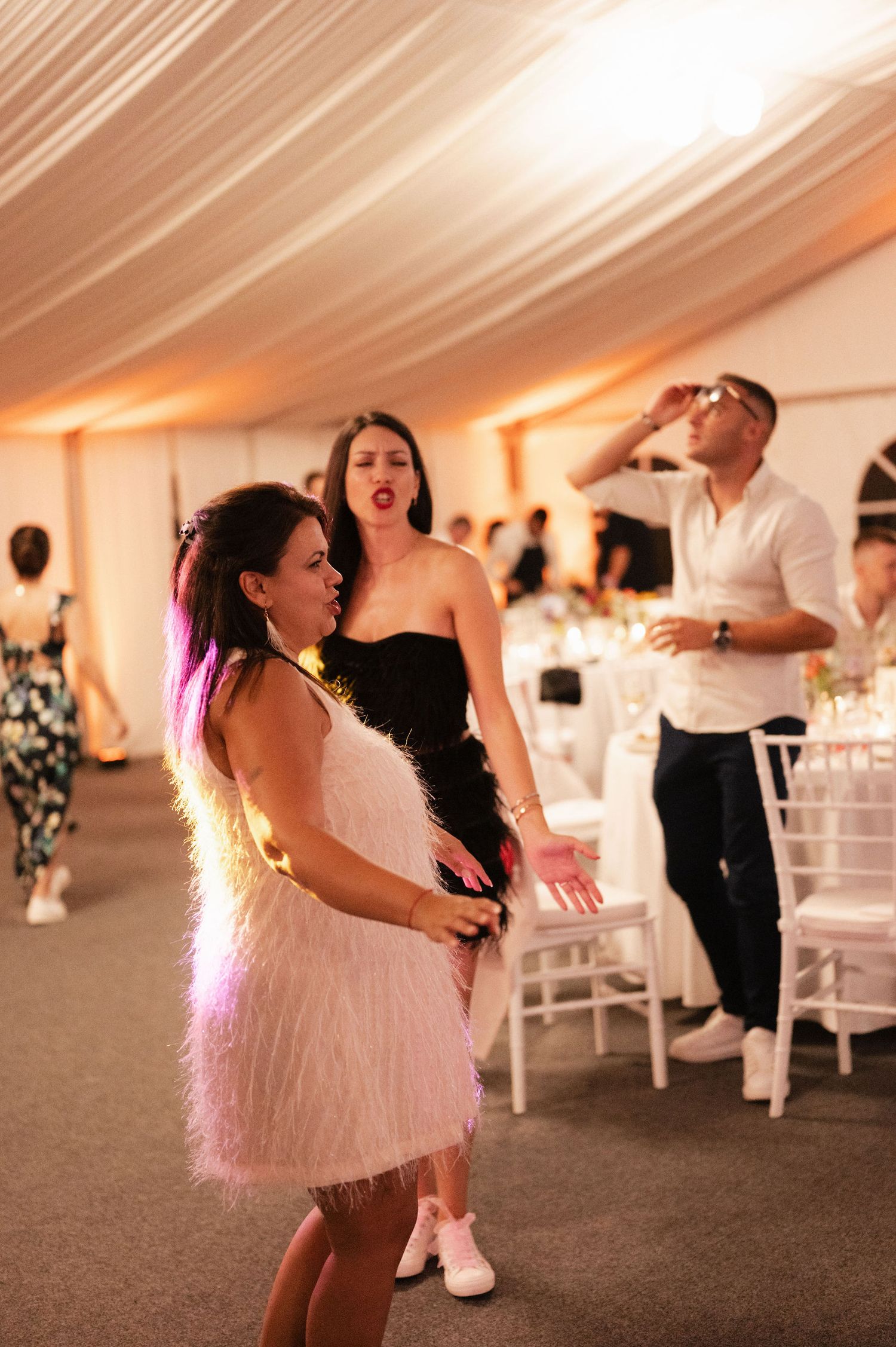 People dancing at a wedding reception in a white tent with soft lighting and decorative elements.