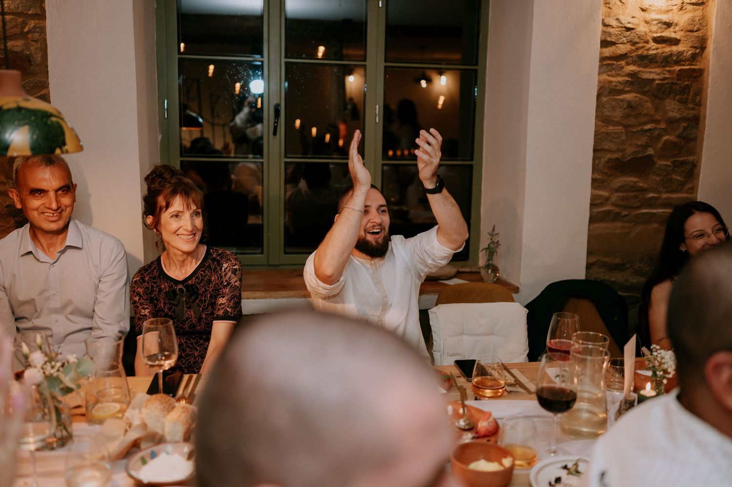 Wedding guests enjoying a lively dinner reception in a rustic venue with exposed brick walls and warm lighting.
