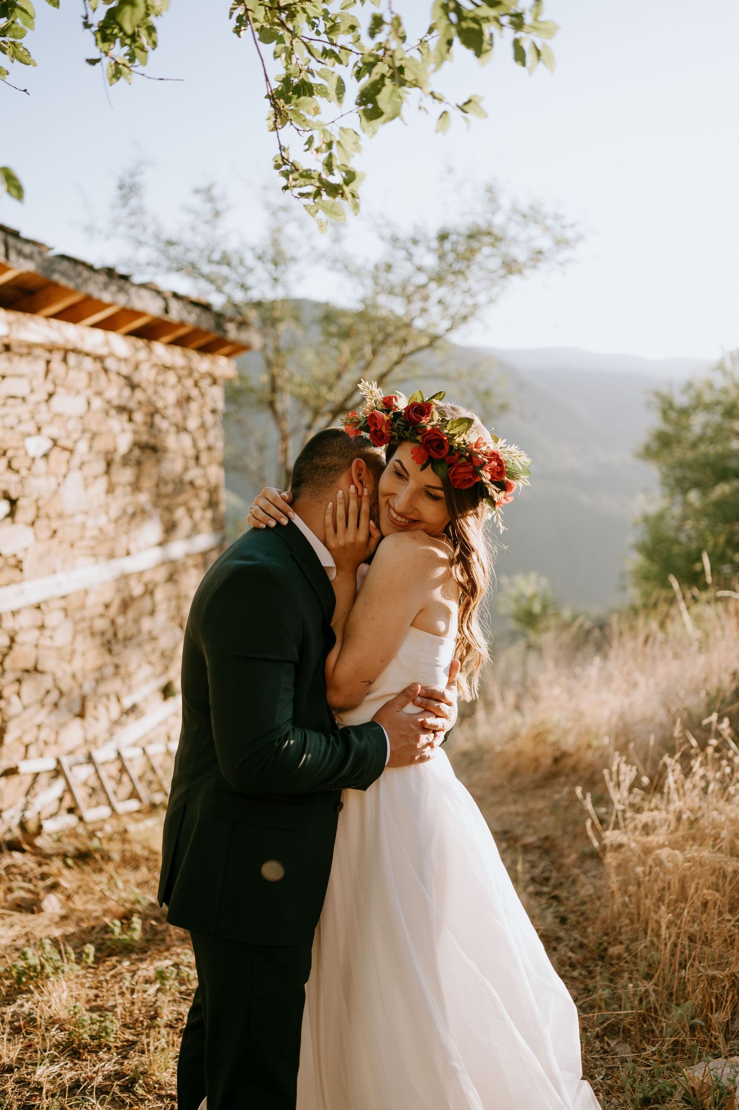 Romantic wedding couple embracing near stone building during golden hour.