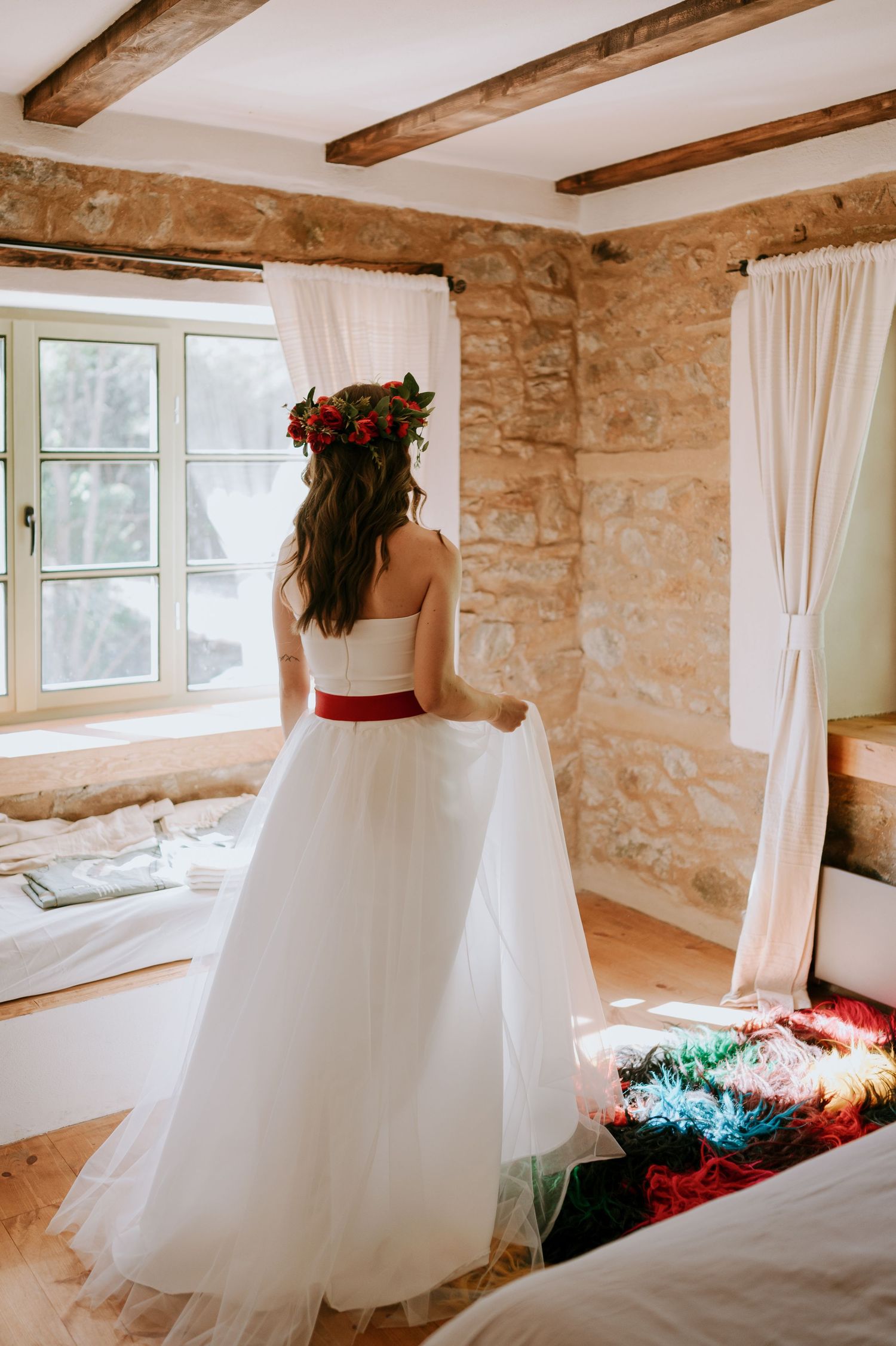Wedding dress with red sash photographed from behind in rustic stone room.