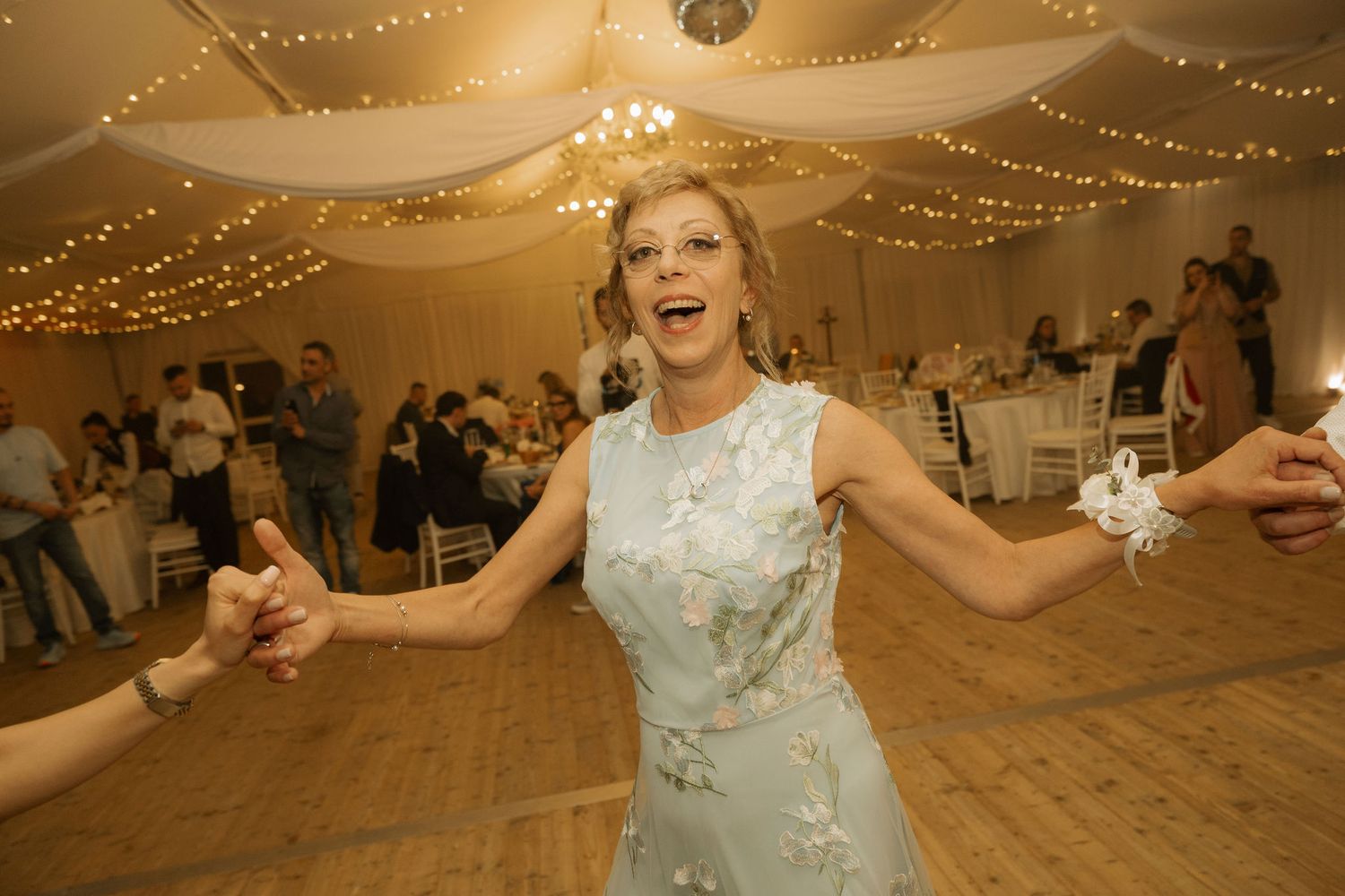 Woman in light blue floral dress dancing joyfully at an elegant wedding reception with fairy lights.