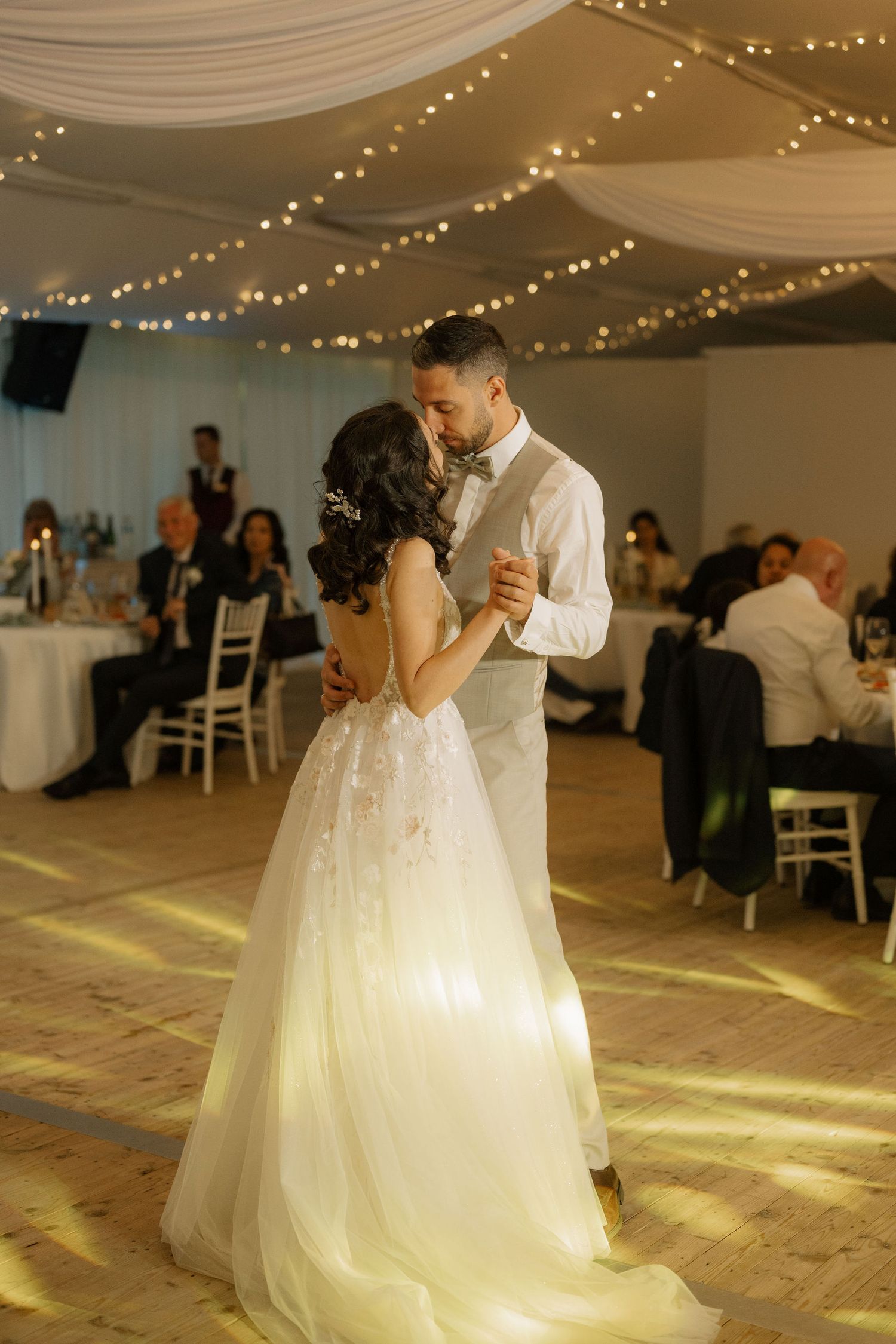 Bride and groom share their first dance under twinkling fairy lights at an elegant wedding reception.