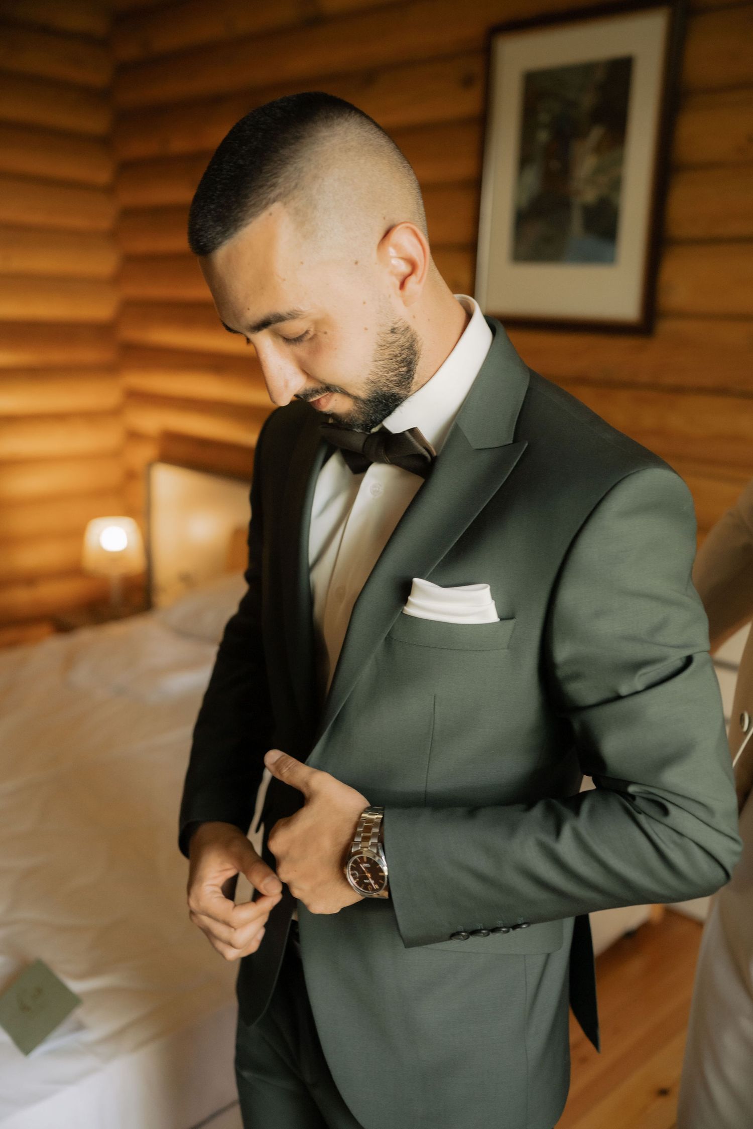 A person in a gray suit adjusts their tie while getting dressed in a wooden-paneled room.