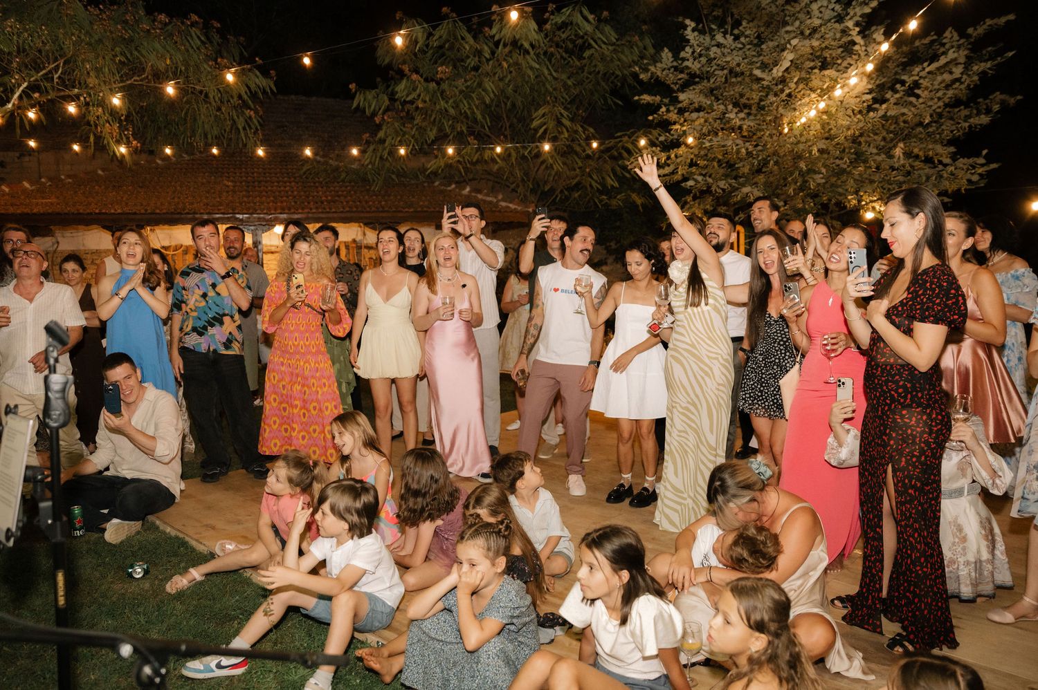 Wedding guests dance and celebrate together during a lively outdoor evening reception under string lights.