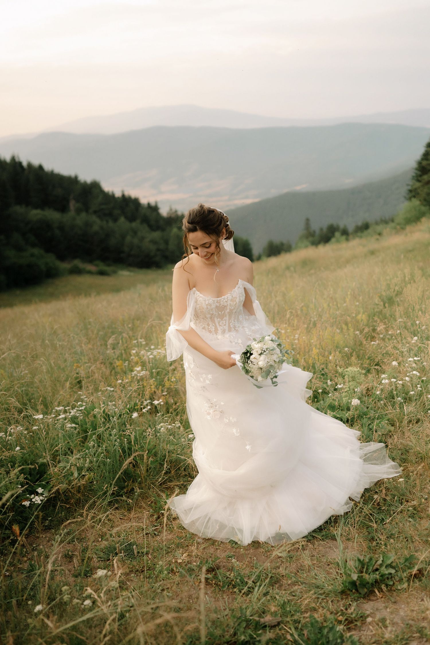An ethereal white bridal gown billows in the breeze against a backdrop of misty mountain peaks and wildflowers.