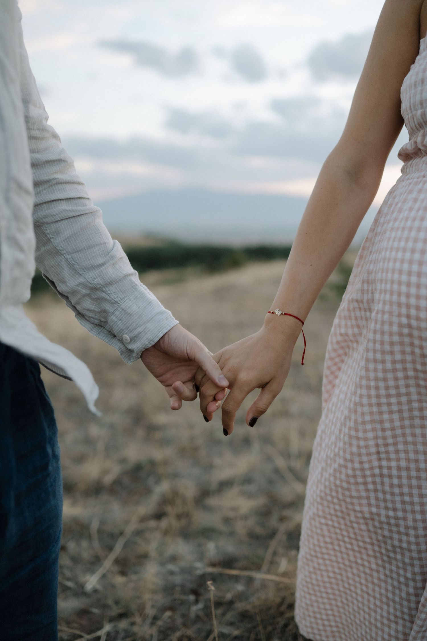 Close-up view of two people holding hands against a blurred outdoor background at sunset.