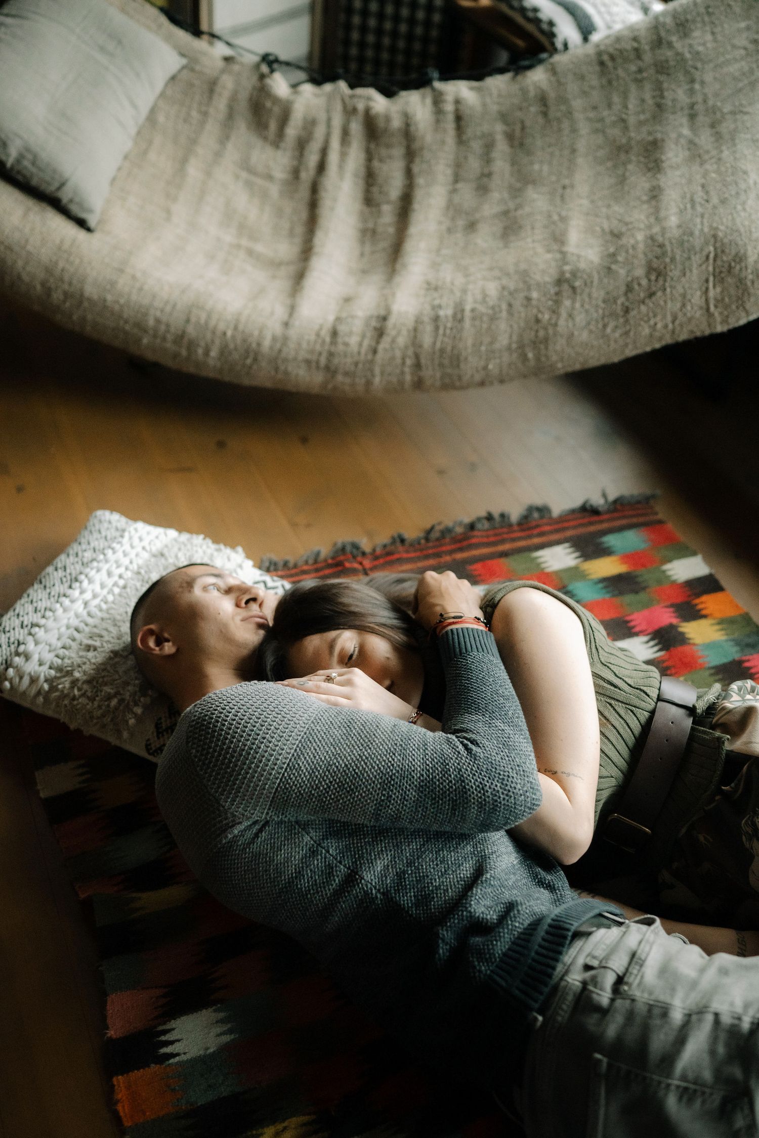 Two people cuddle close together while resting on a colorful patterned rug in a cozy indoor setting.